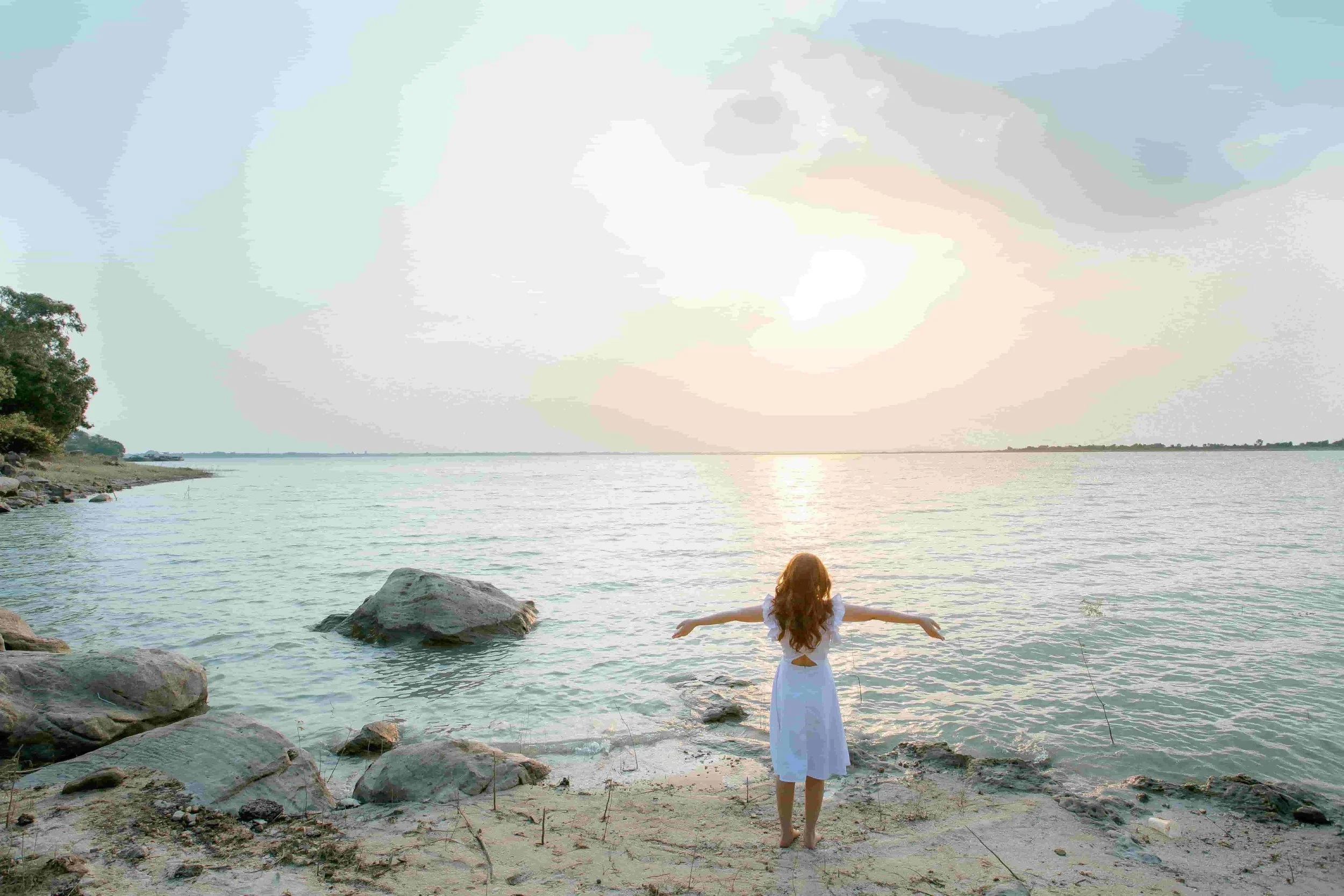 A woman standing by the ocean at sunrise, embracing calm and self-reflection through individual therapy and emotional healing.