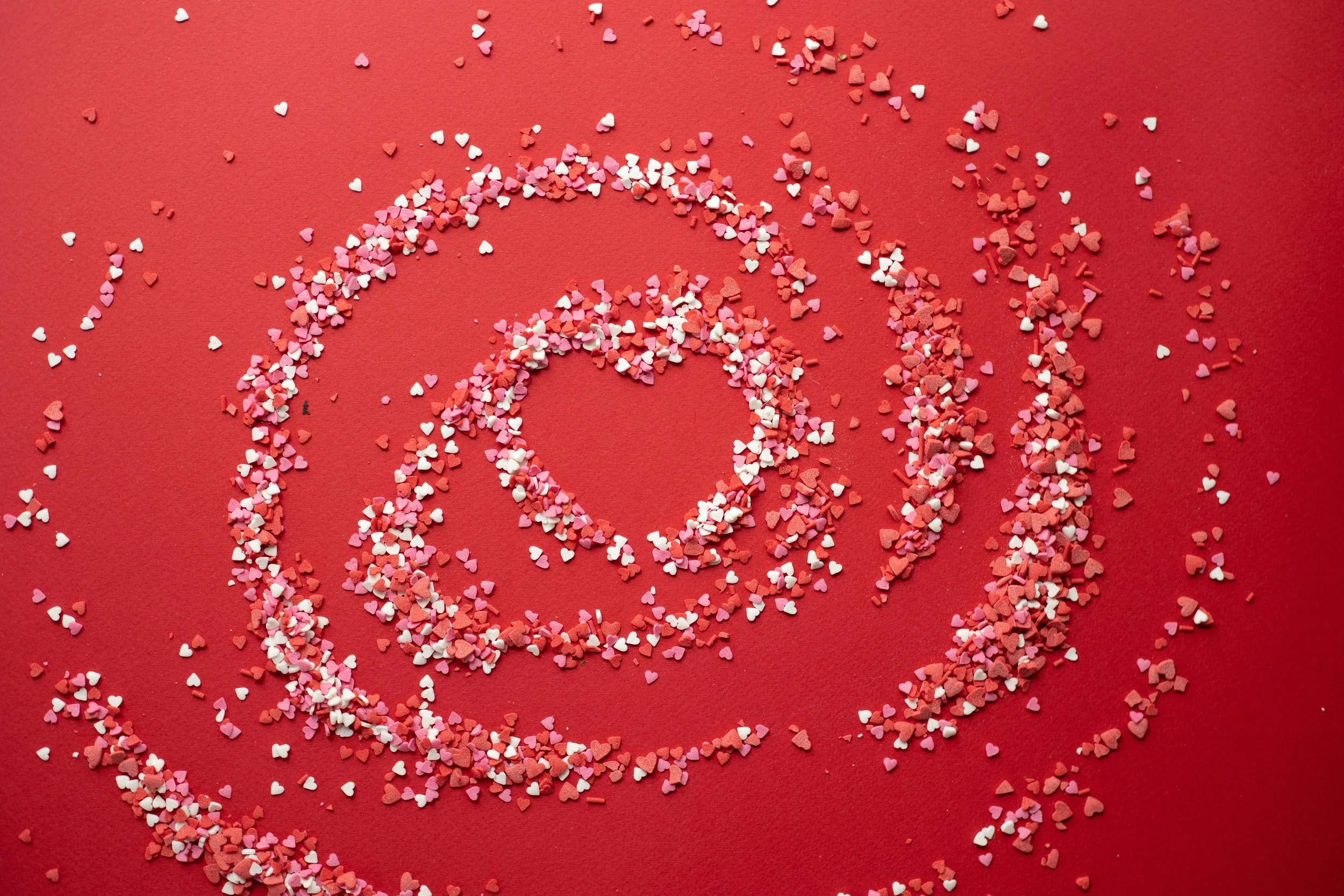 Heart-shaped sprinkles forming a spiral pattern on a red background, symbolizing the emotional swirl of dating with an anxious attachment style