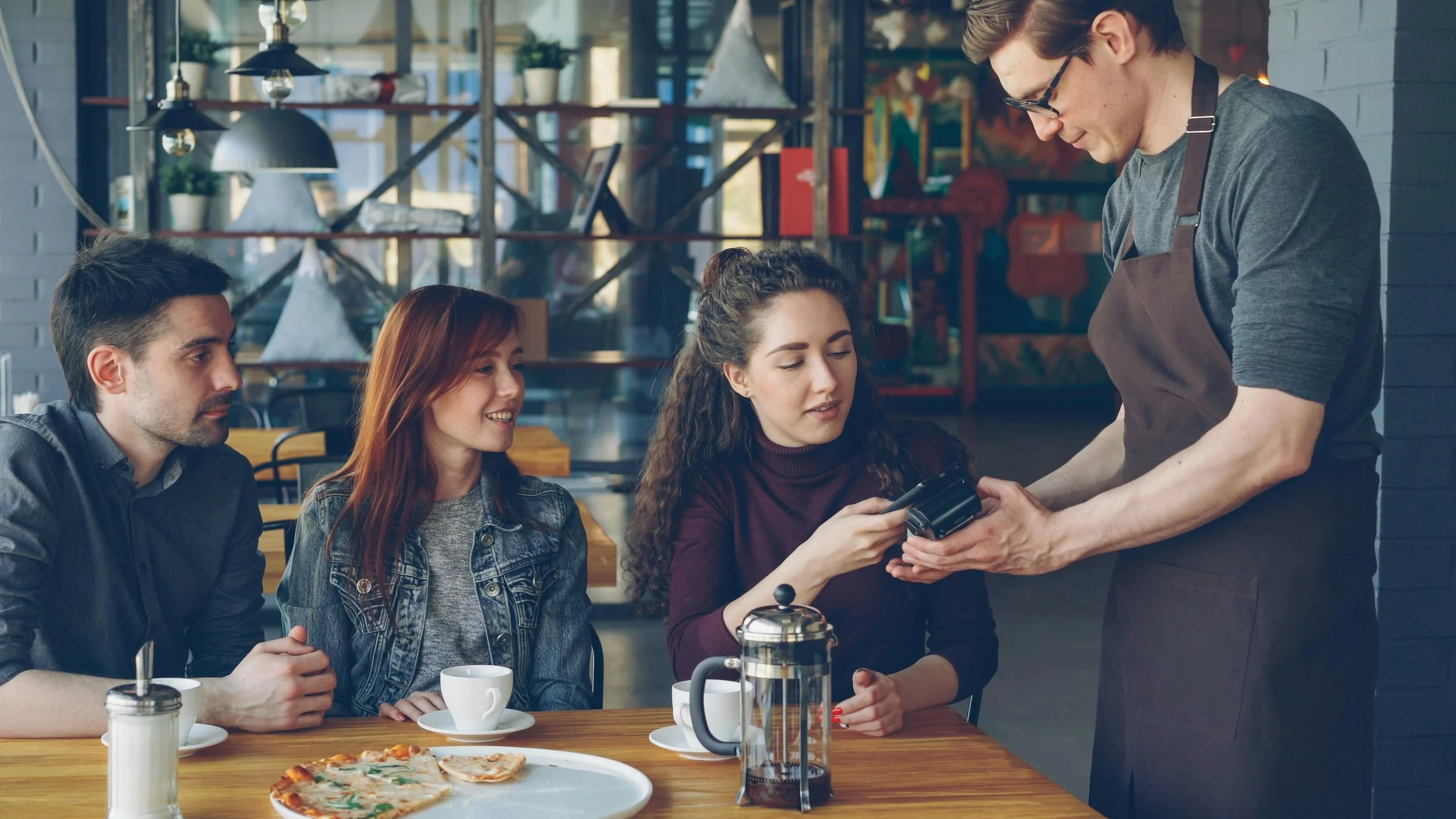 Group dining at restaurant while woman pays the bill, reflecting financial control, independence, and discomfort receiving support.