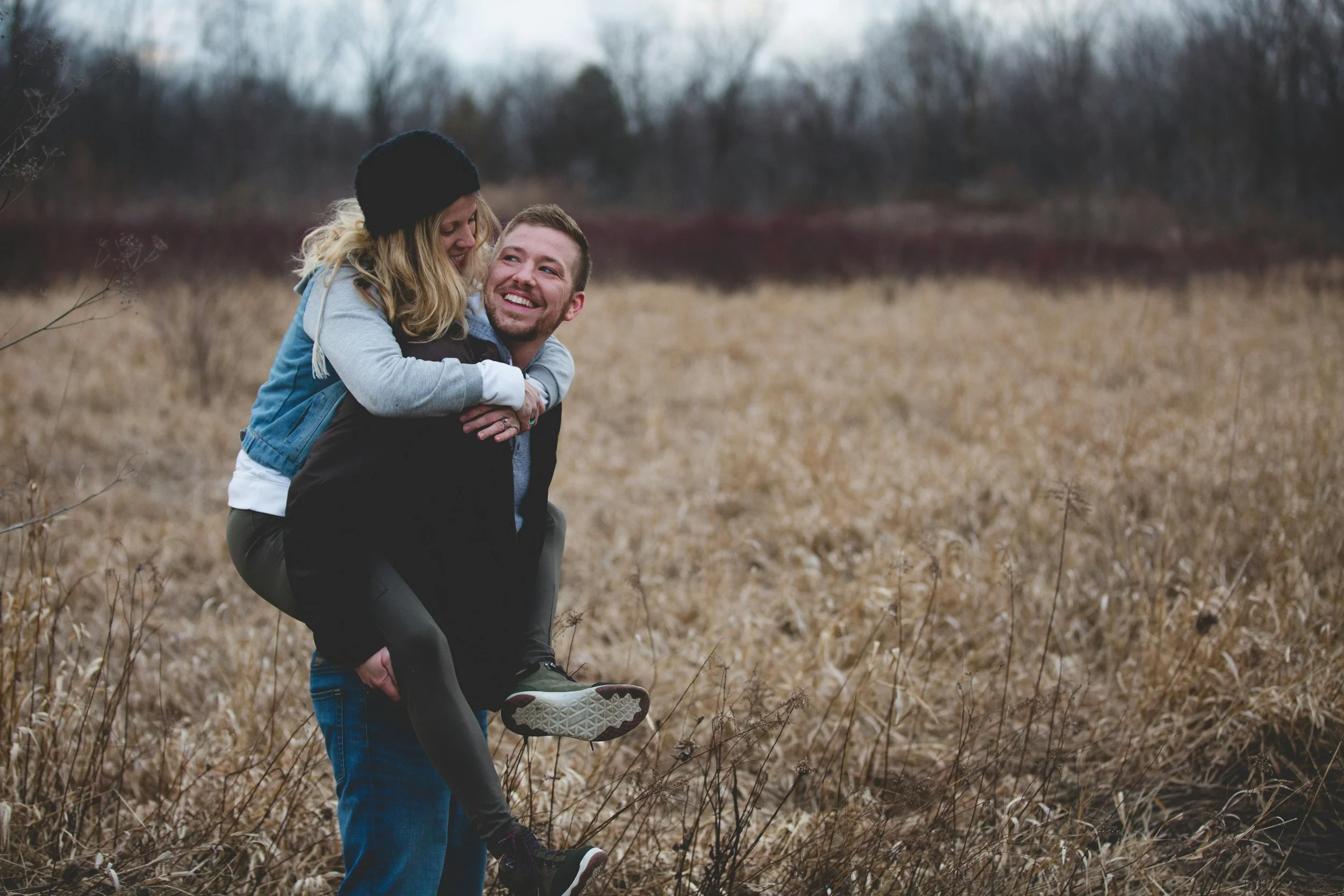Couple laughing in an open field with piggyback pose, capturing connection and intimacy in dating while navigating relationship choices and future compatibility.