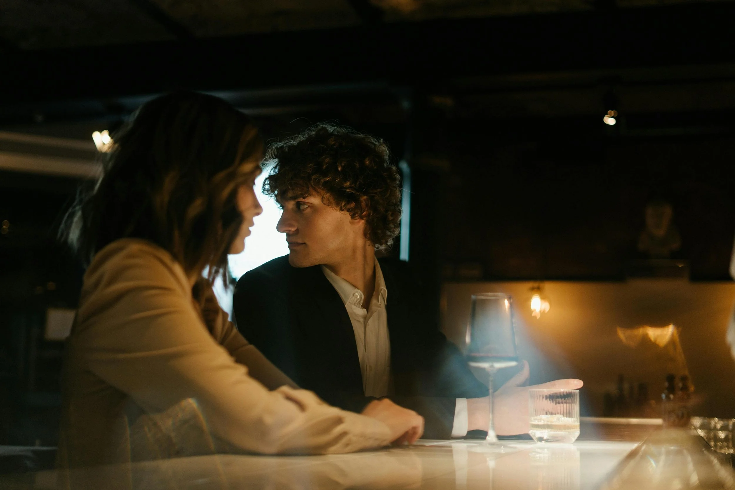 Couple sitting closely at a dimly lit bar during a serious conversation, representing hyper-independent women navigating emotional responsibility, over-functioning, and relationship dynamics in dating.