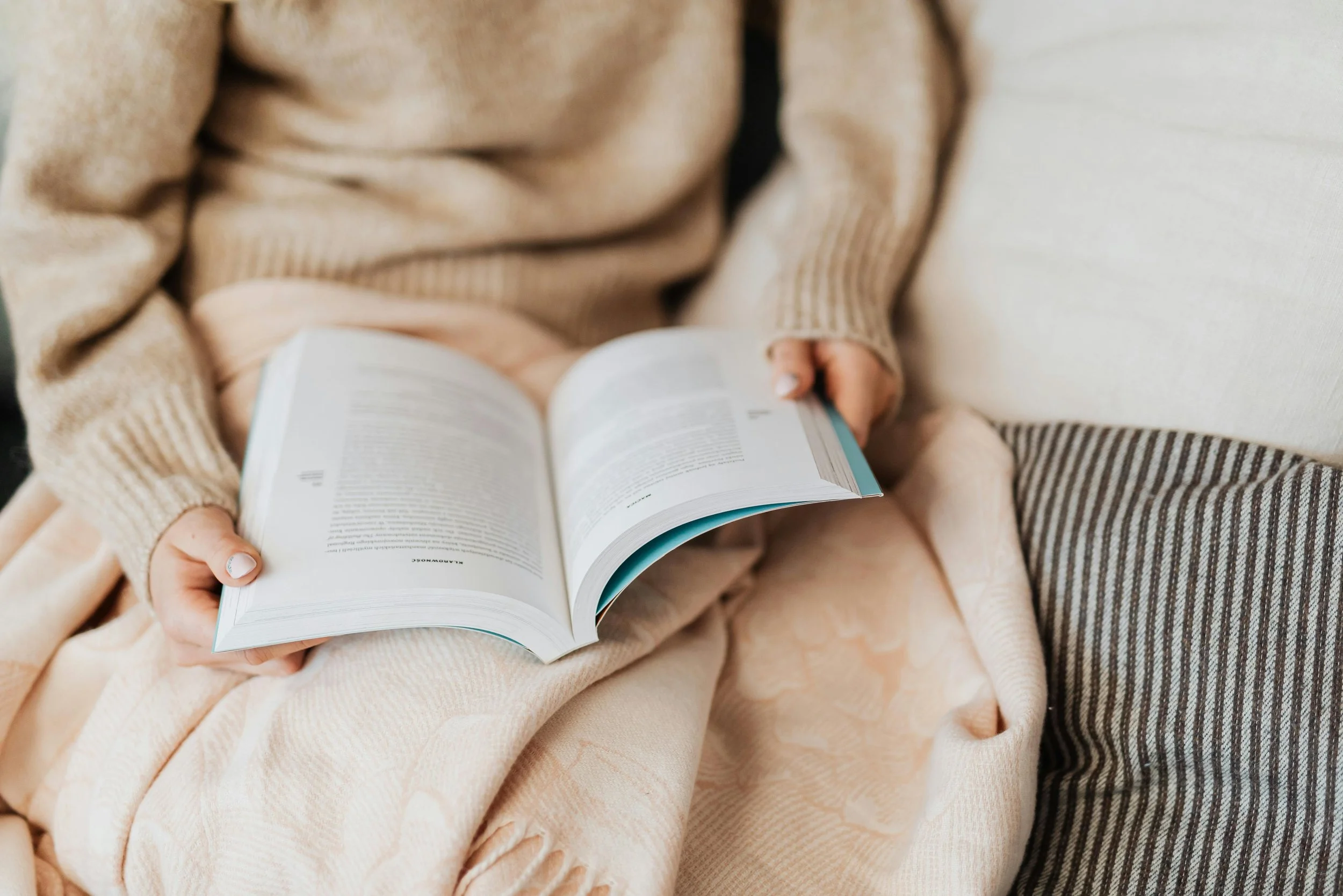 Person reading a book wrapped in a blanket, representing fandom, emotional attachment to stories, fictional relationships, and the search for connection and understanding.