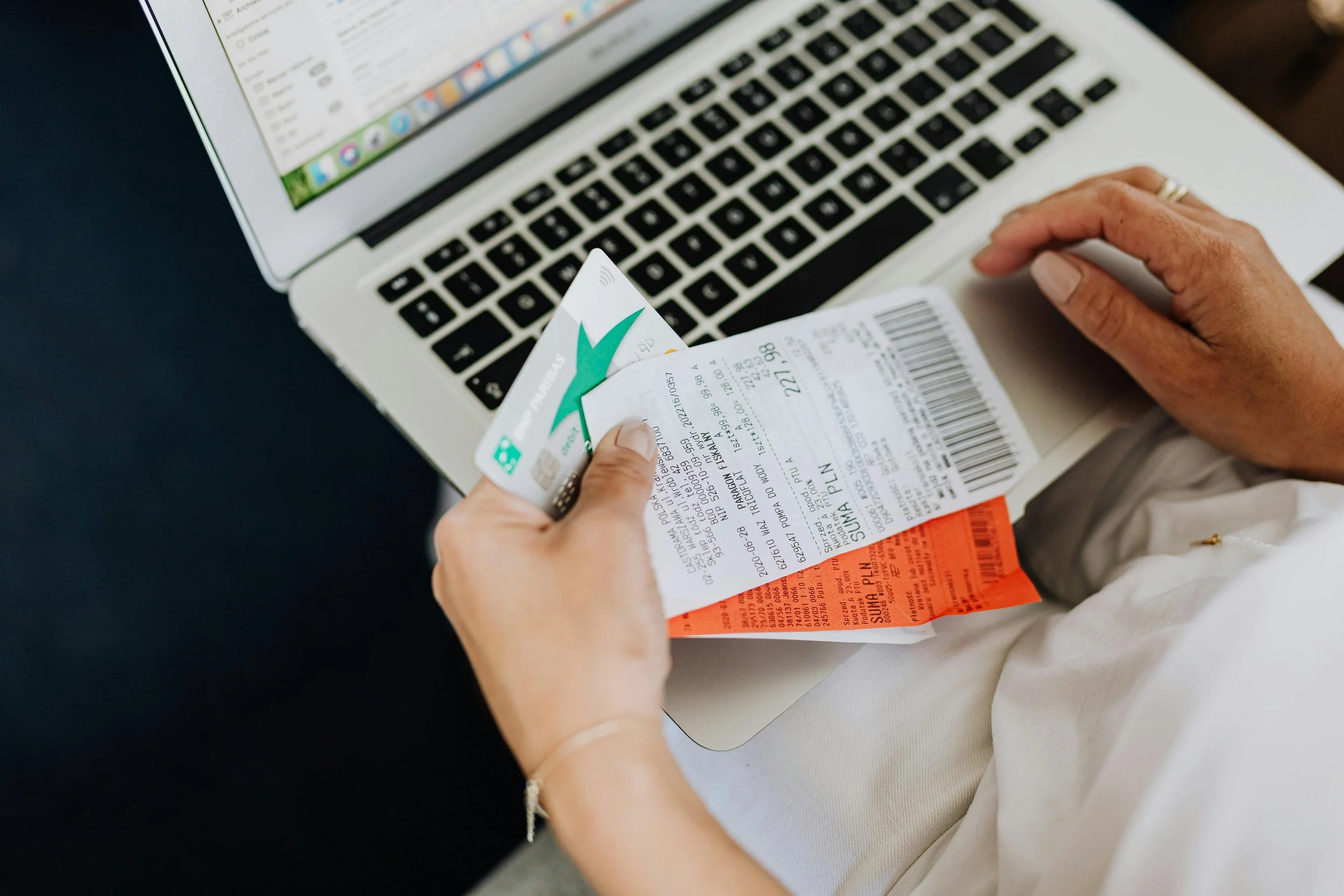 Woman holding receipts and credit card while reviewing finances on laptop, representing financial control and hyper-independence behaviors.