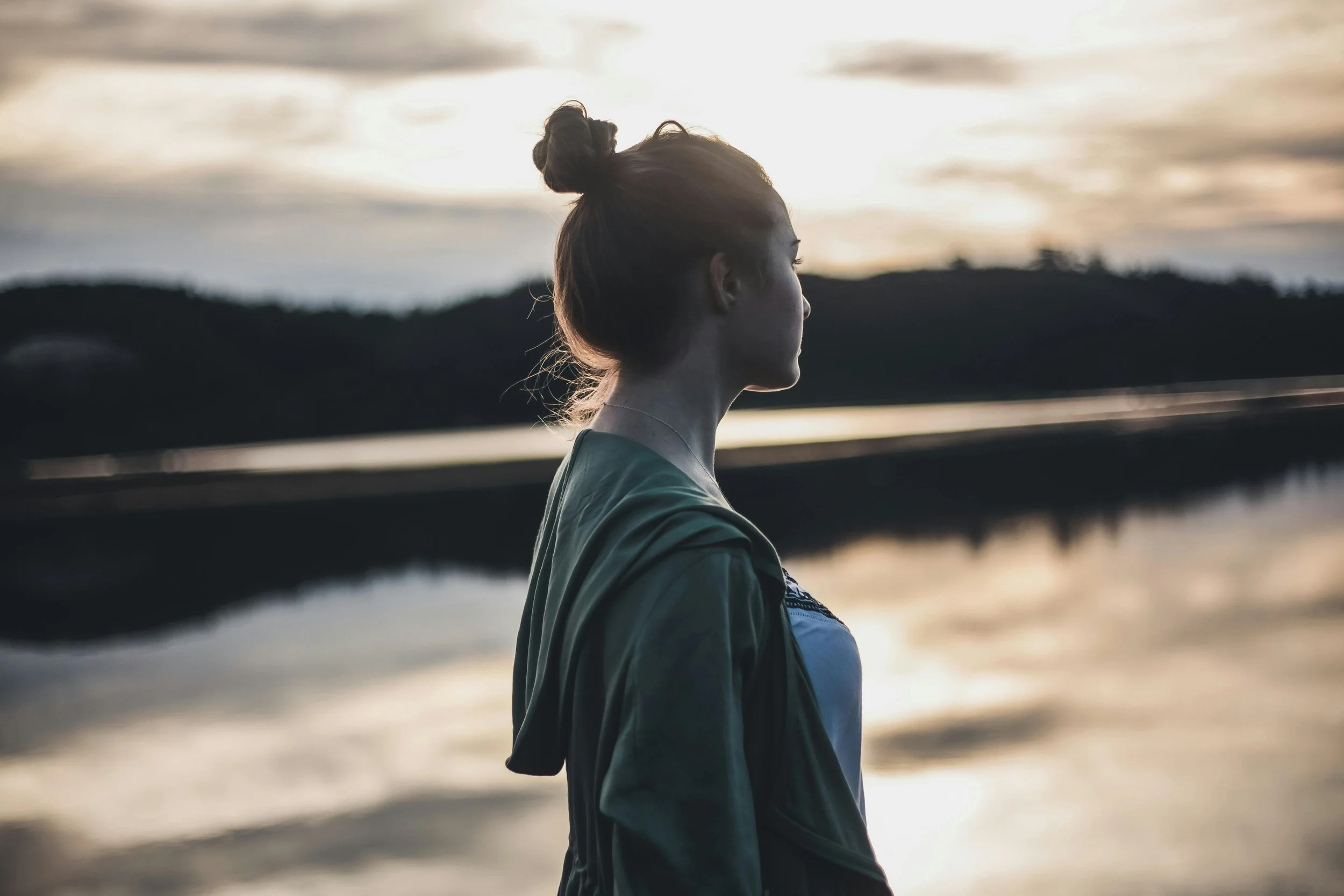Woman standing alone by the water at sunset, reflecting on sadness, emotional exhaustion, and suppressed anger connected to the oldest daughter role.