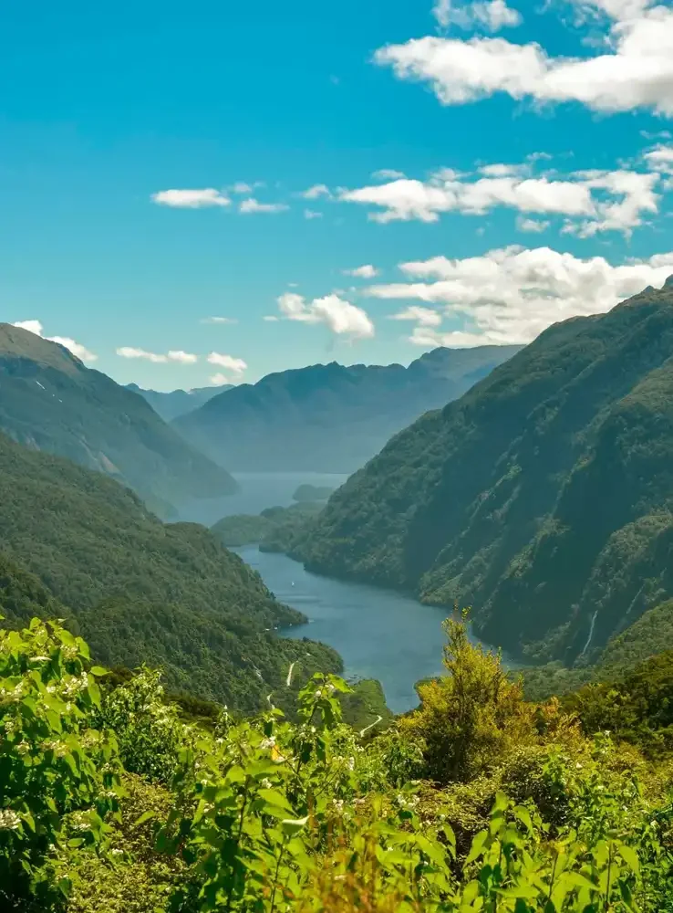 A scenic view of a river winding through lush green mountains under a blue sky with scattered clouds.