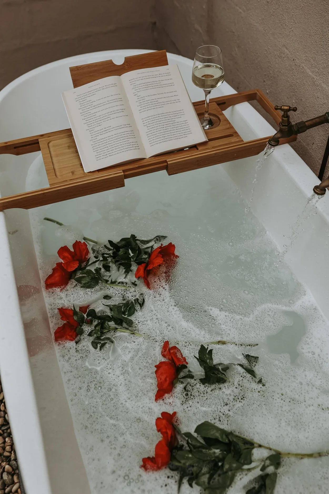 Outdoor freestanding bath with red flowers, open book and wine glass, private courtyard, Braithwaite Hobart Sandy Bay Tasmania