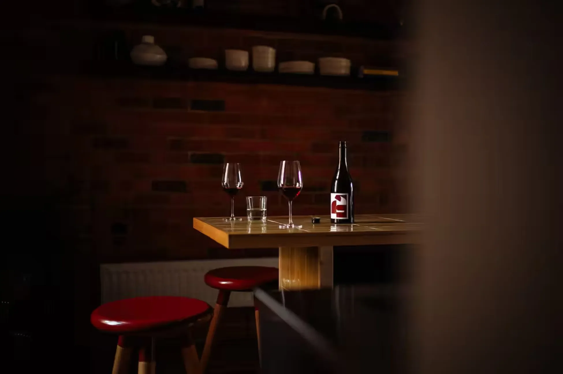 Two glasses of red wine and bottle on wooden table with red stools, intimate brick-walled interior of Ogee restaurant North Hobart Tasmania