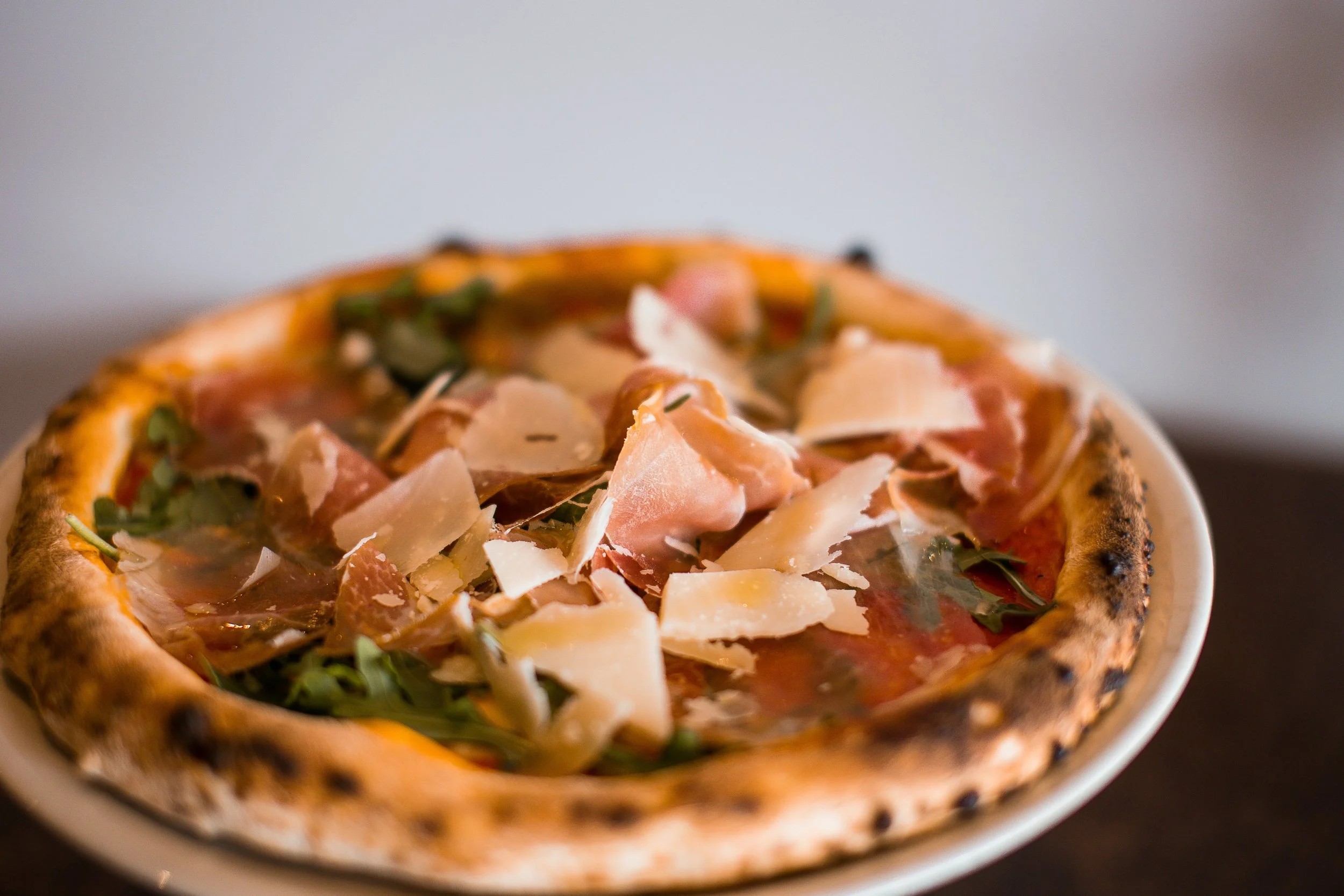 Stone-baked pizza topped with prosciutto, arugula, and shaved Parmesan cheese.