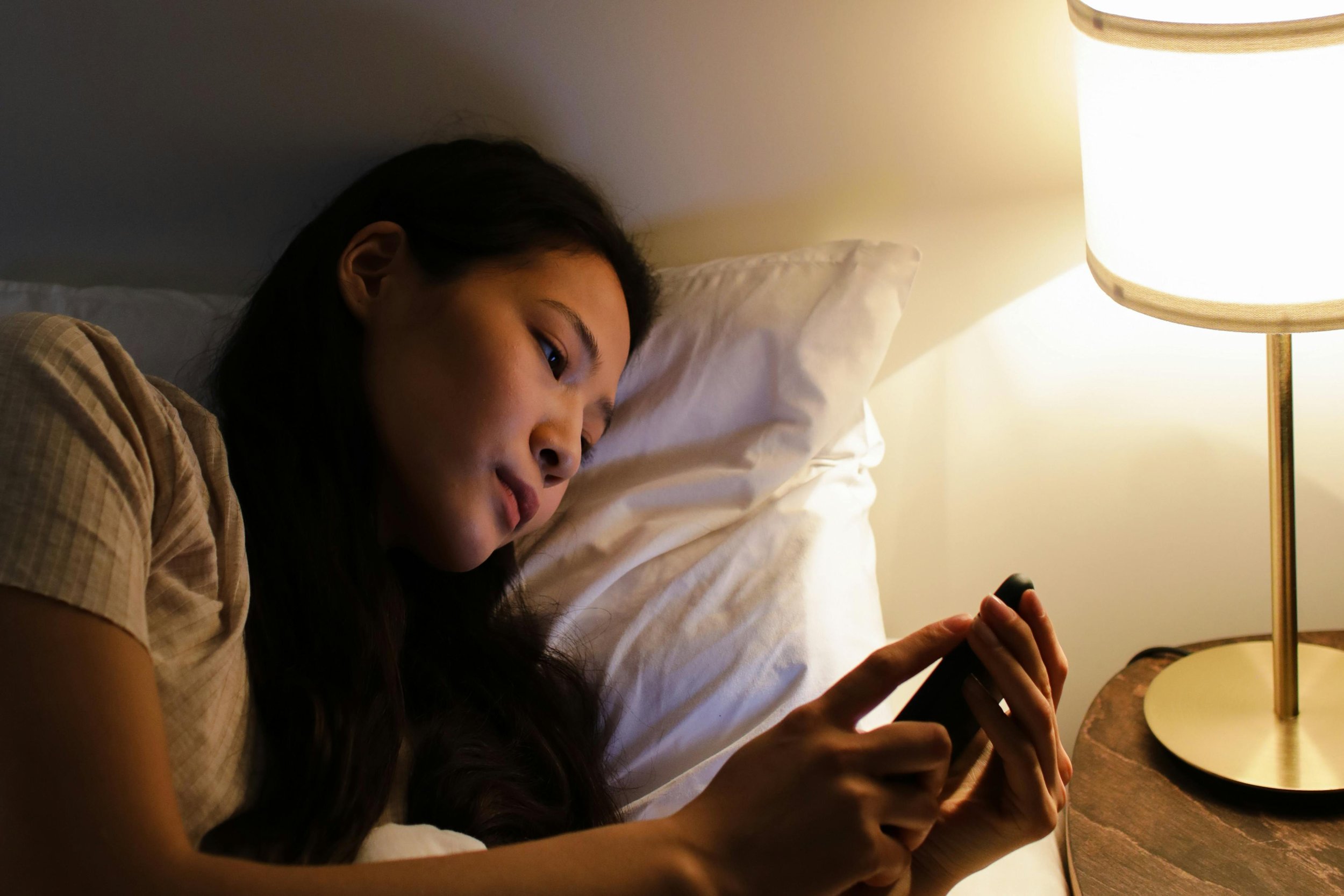 image of a woman with black hair on her phone in bed representing anxiety and OCD. Find relief today with therapy for OCD in Sacramento