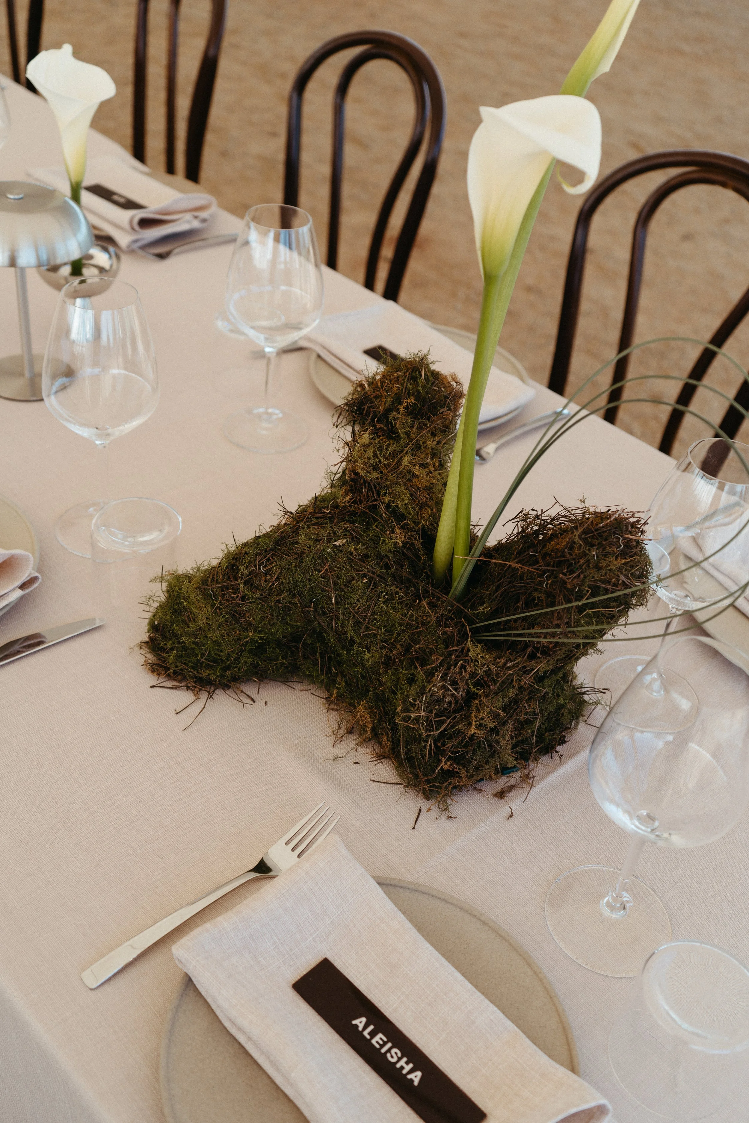 Table centerpiece with moss, twigs, and a tall white calla lily flower at a formal dining event.