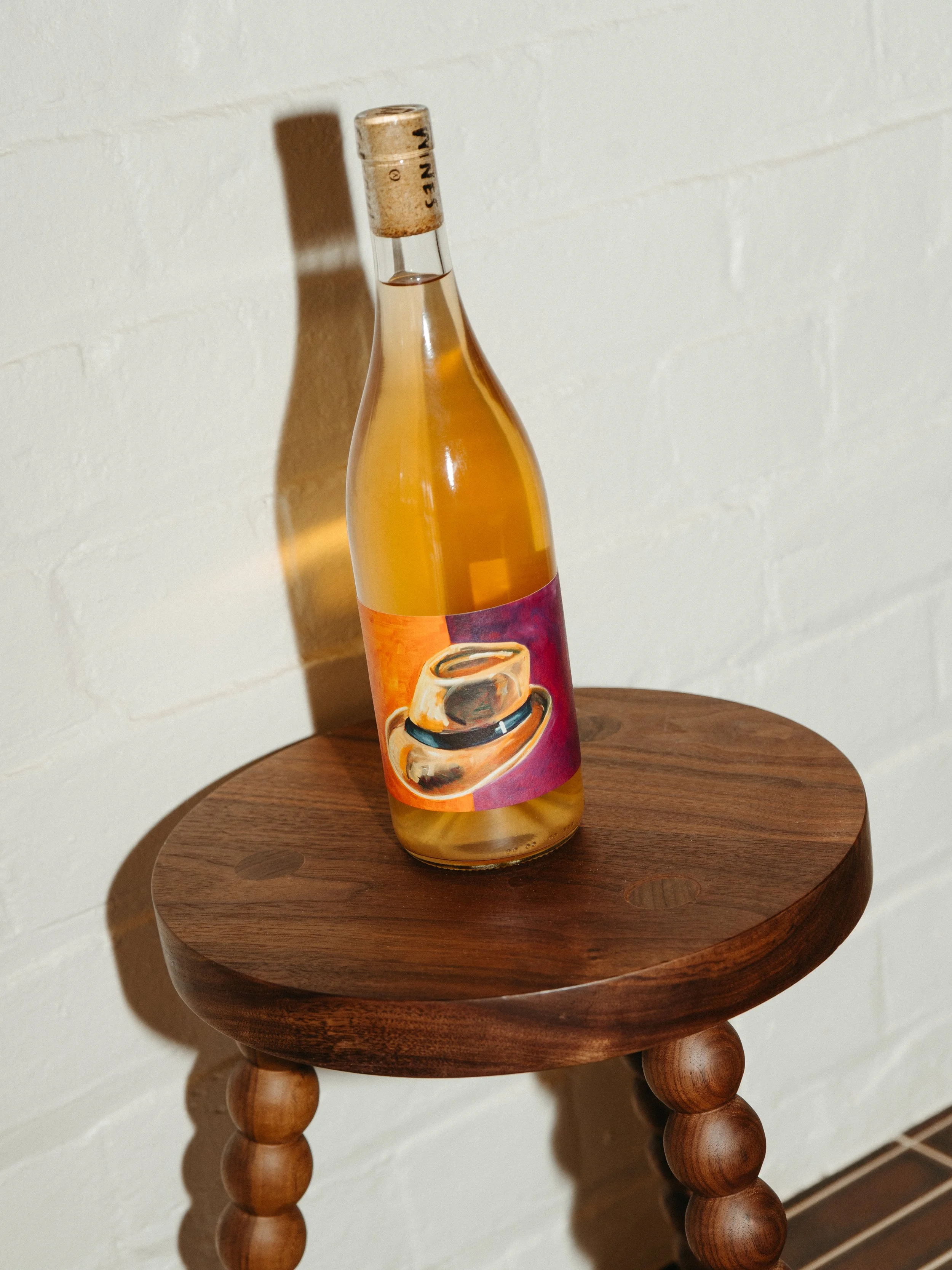 A glass bottle with a colorful label featuring a coffee cup, placed on a round wooden side table against a white brick wall.