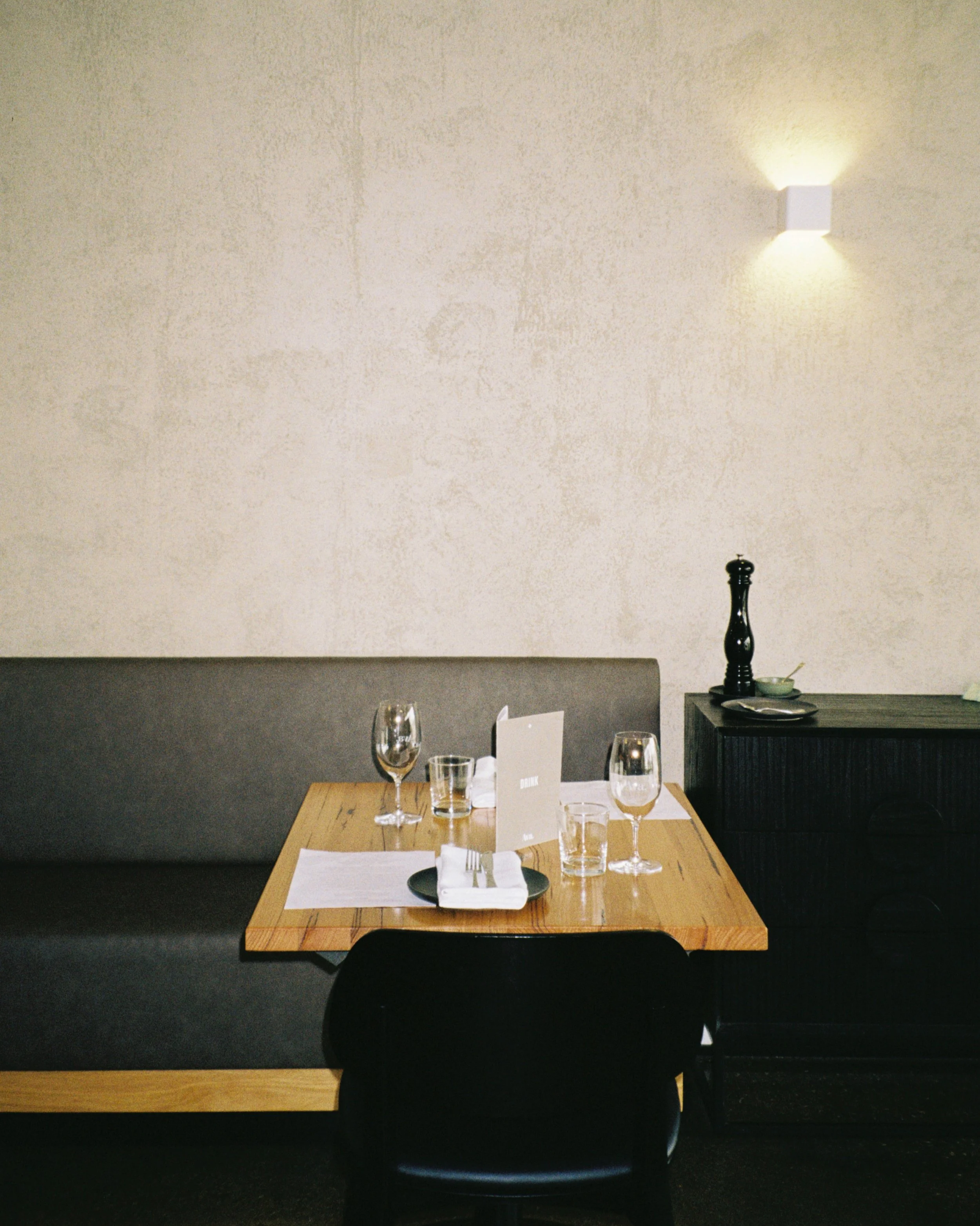 Empty restaurant table with glassware and menu, against a textured beige wall with a small wall sconce light.