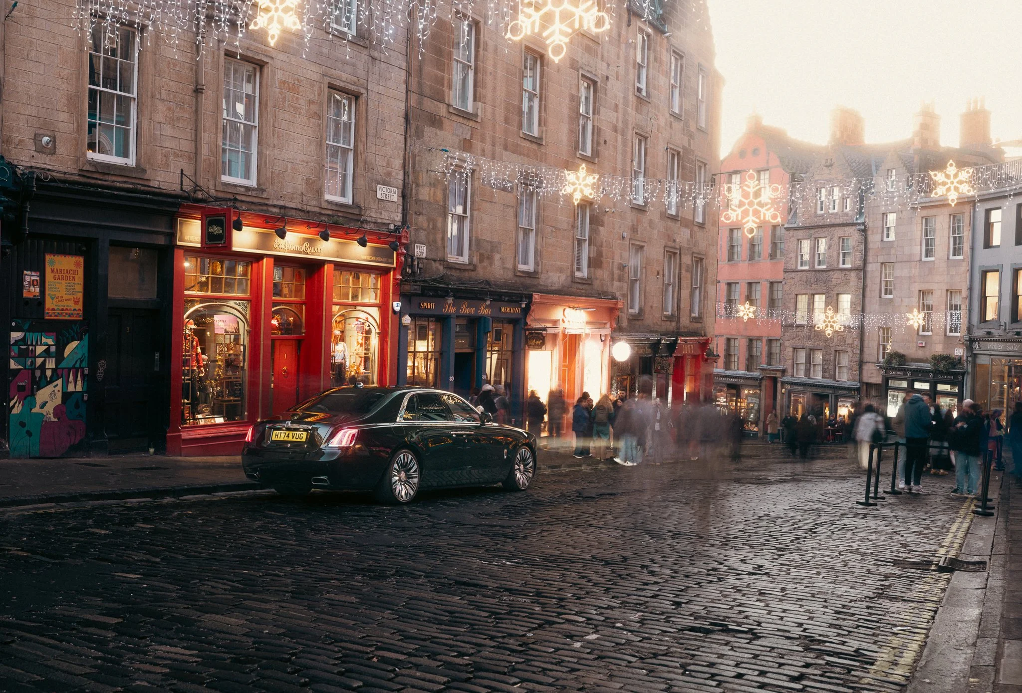 A Rolls Royce Ghost parked on a cobbled Edinburgh street with passers by and Christmas lights