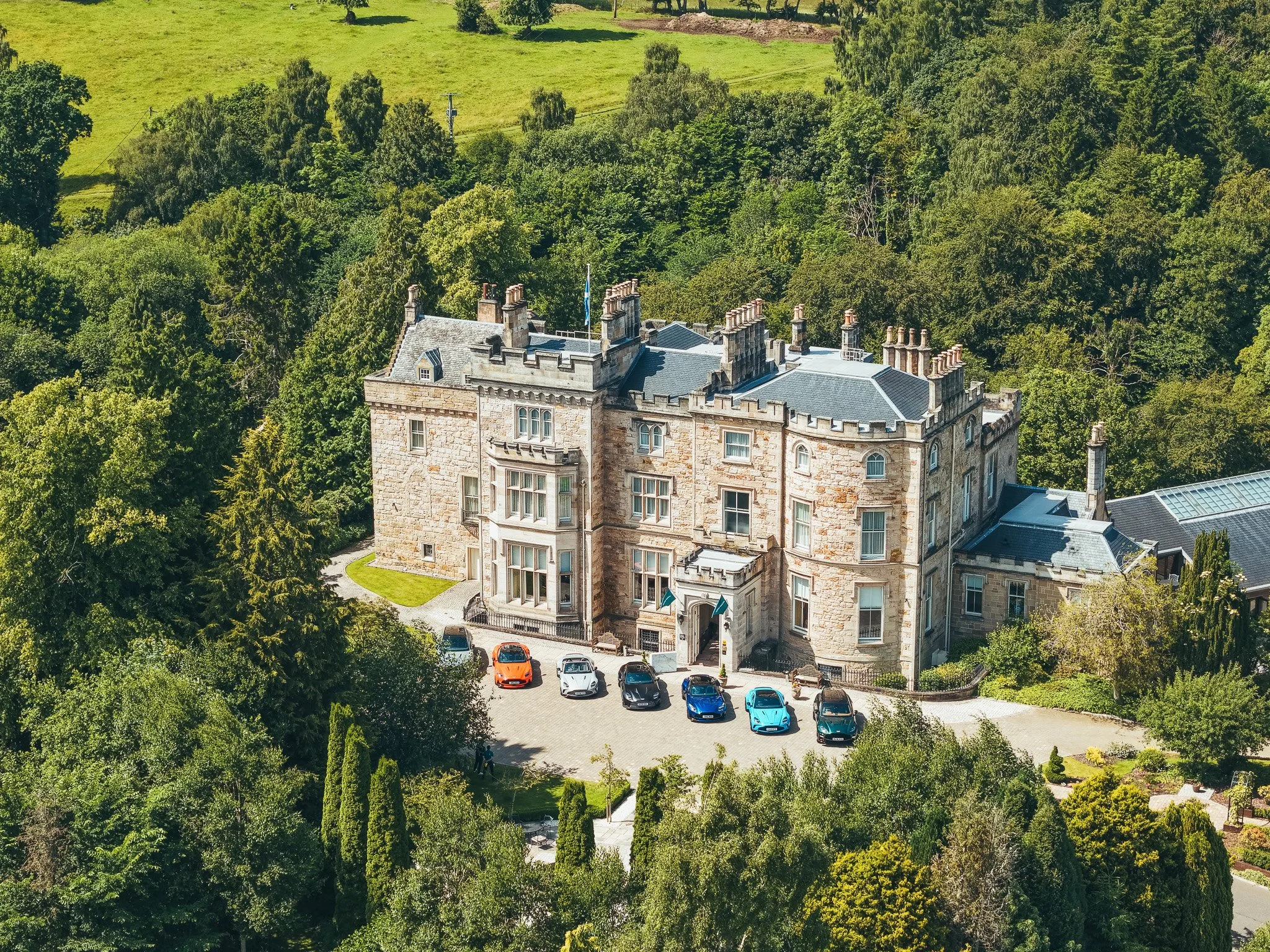 A lineup of Aston Martin cars parked outside a large estate house