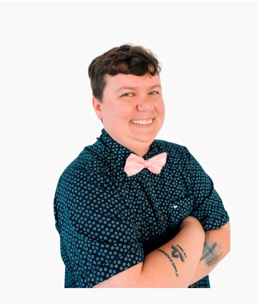 Black and white portrait of a smiling person with short curly hair, wearing a patterned button-up shirt, standing against a plain wall.