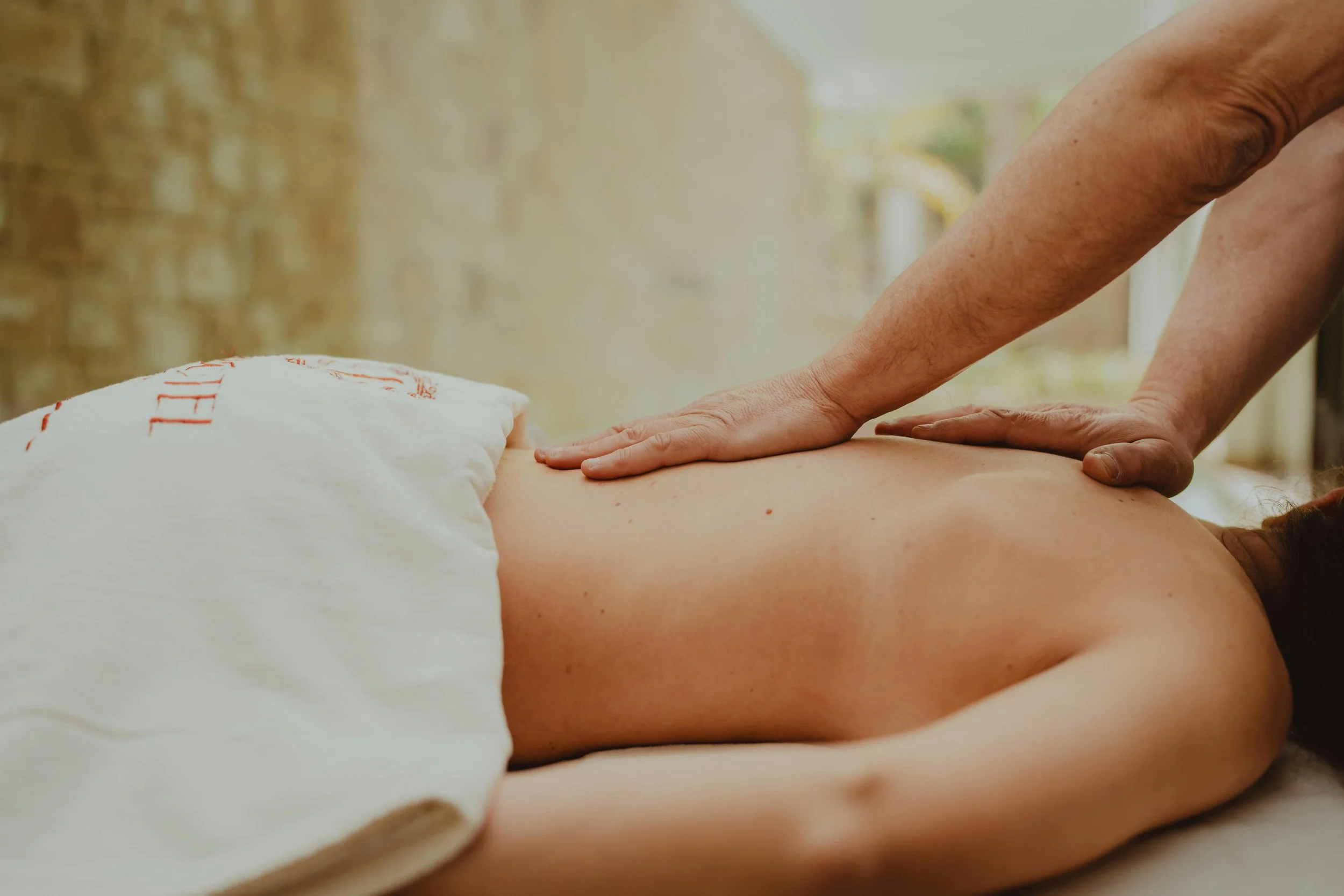 Person receiving a massage or physiotherapy session, lying face down on a treatment table with a therapist applying pressure to their back.