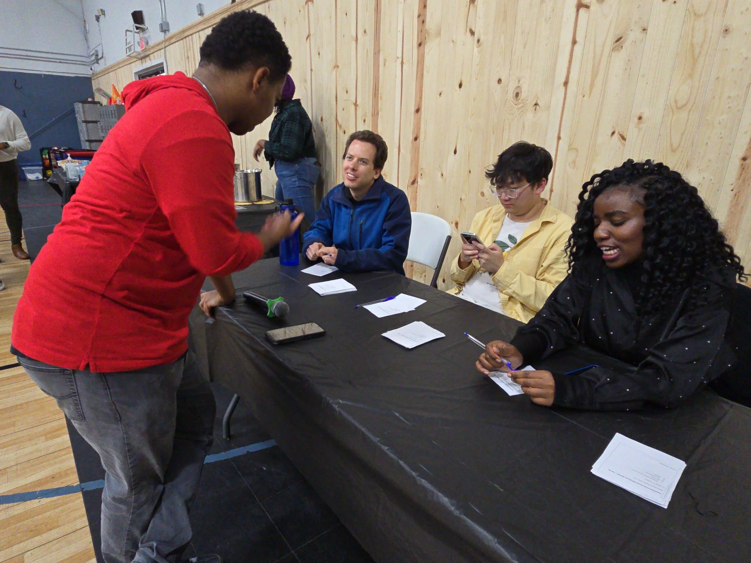 Four people sitting and talking at a table during an event, with one person standing and engaging with the seated individuals.
