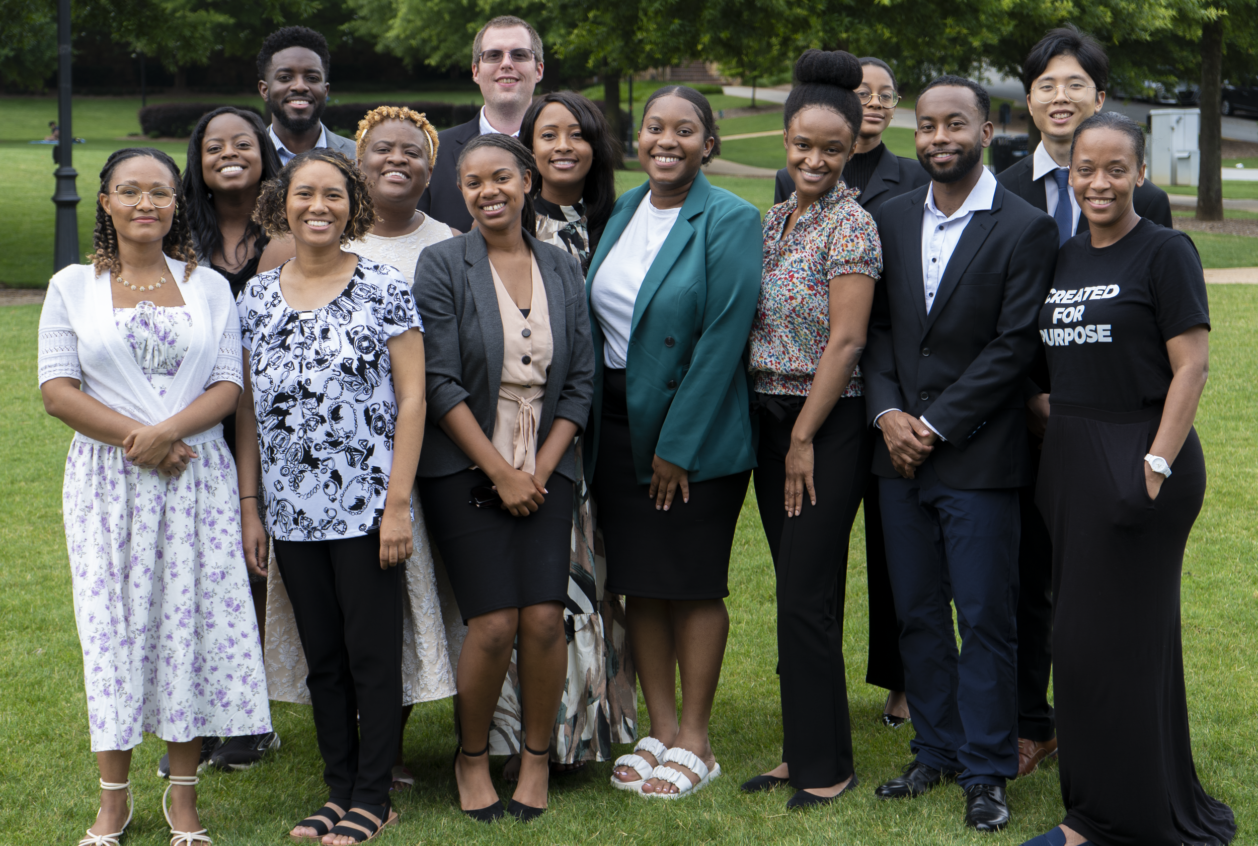 Group of diverse professionals posing outdoors in a park, standing on grass with trees in the background.