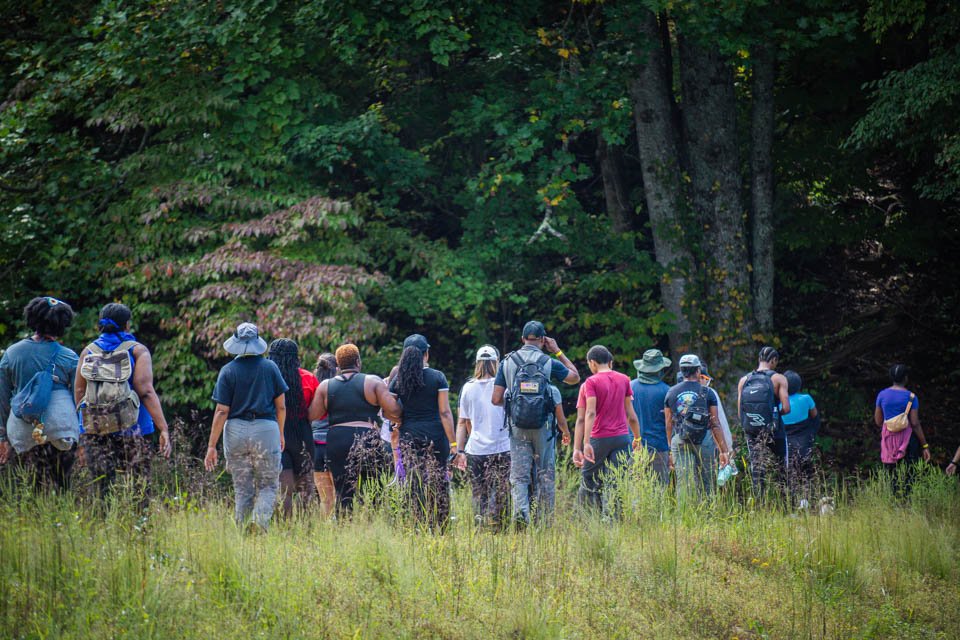 Group of people walking through a grassy, wooded area during daytime.
