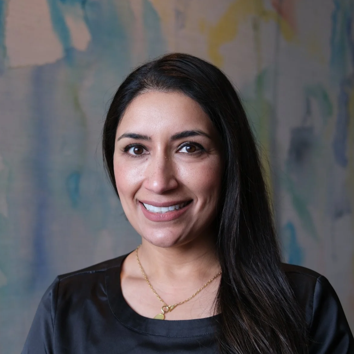 Dr. Nimrit Gill smiling in front of a white, blue, yellow backdrop