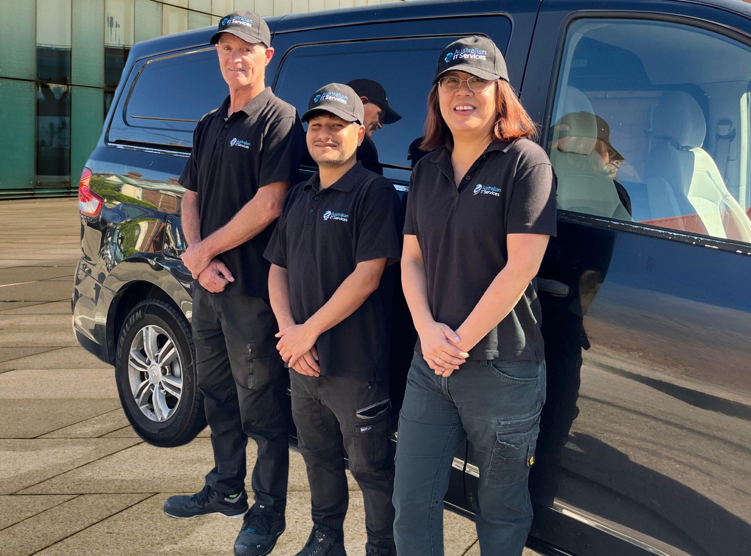 Three Australian IT Services Technical Cleaners standing in front of a black van, wearing matching black polo shirts and caps with the logo 'Australian IT Services'.