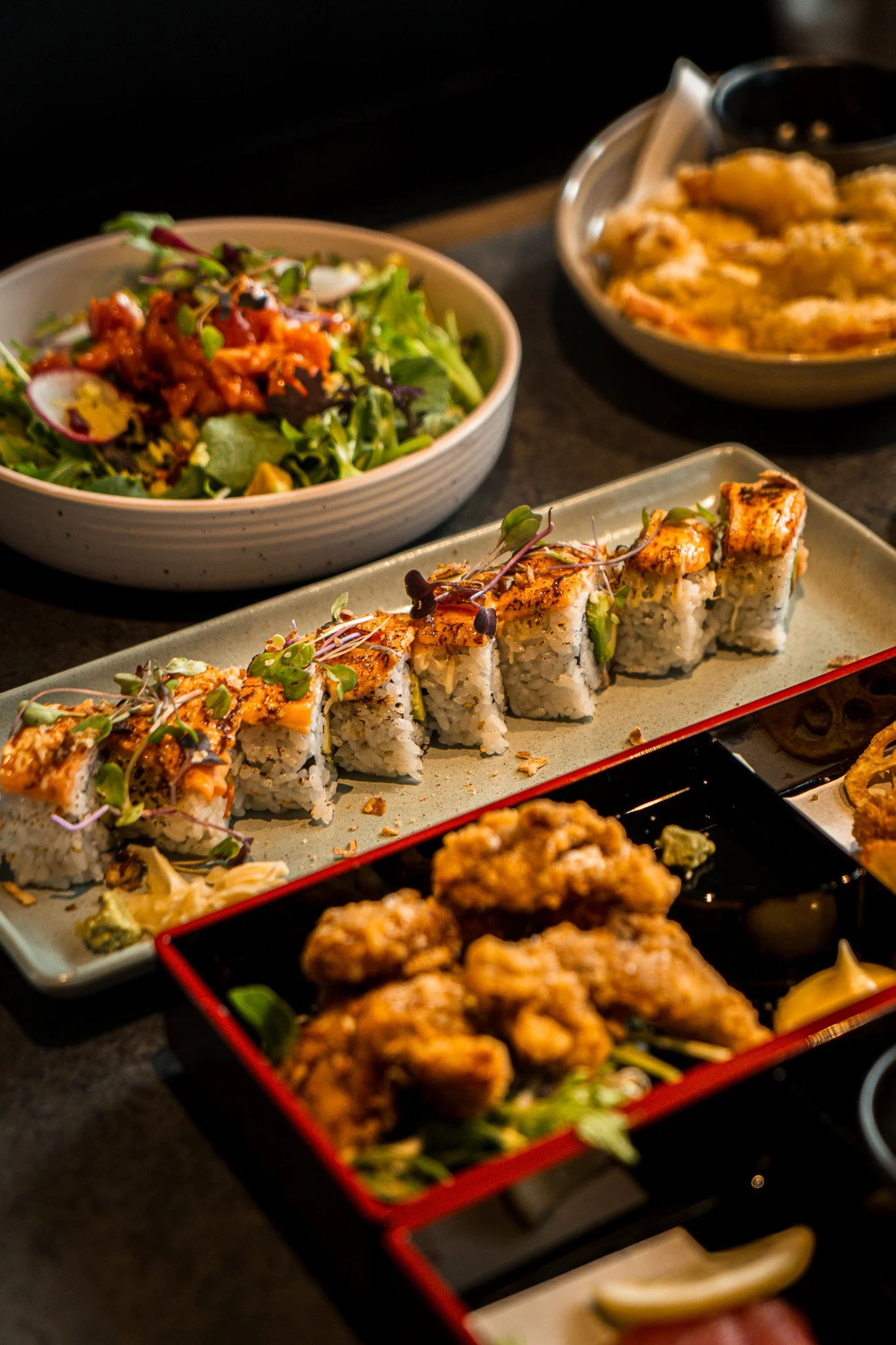 Assorted Japanese dishes including sushi rolls, fried chicken, a salad, and bowls of tempura and other side dishes on a table.