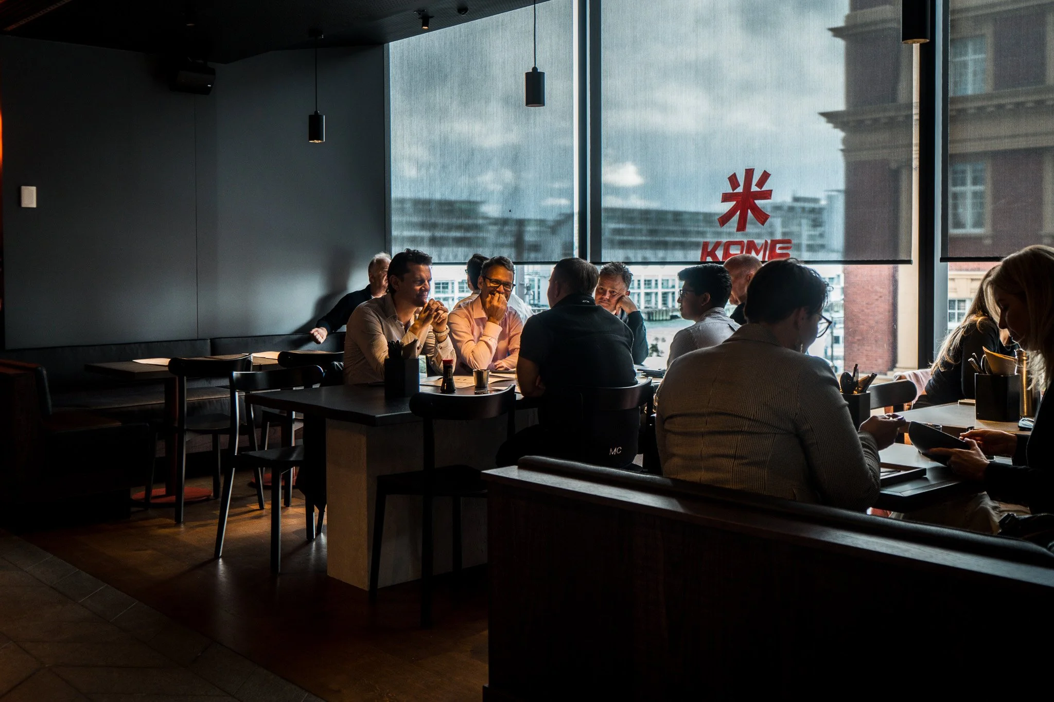 People sitting at tables inside a restaurant or cafe with large window showing city buildings outside.