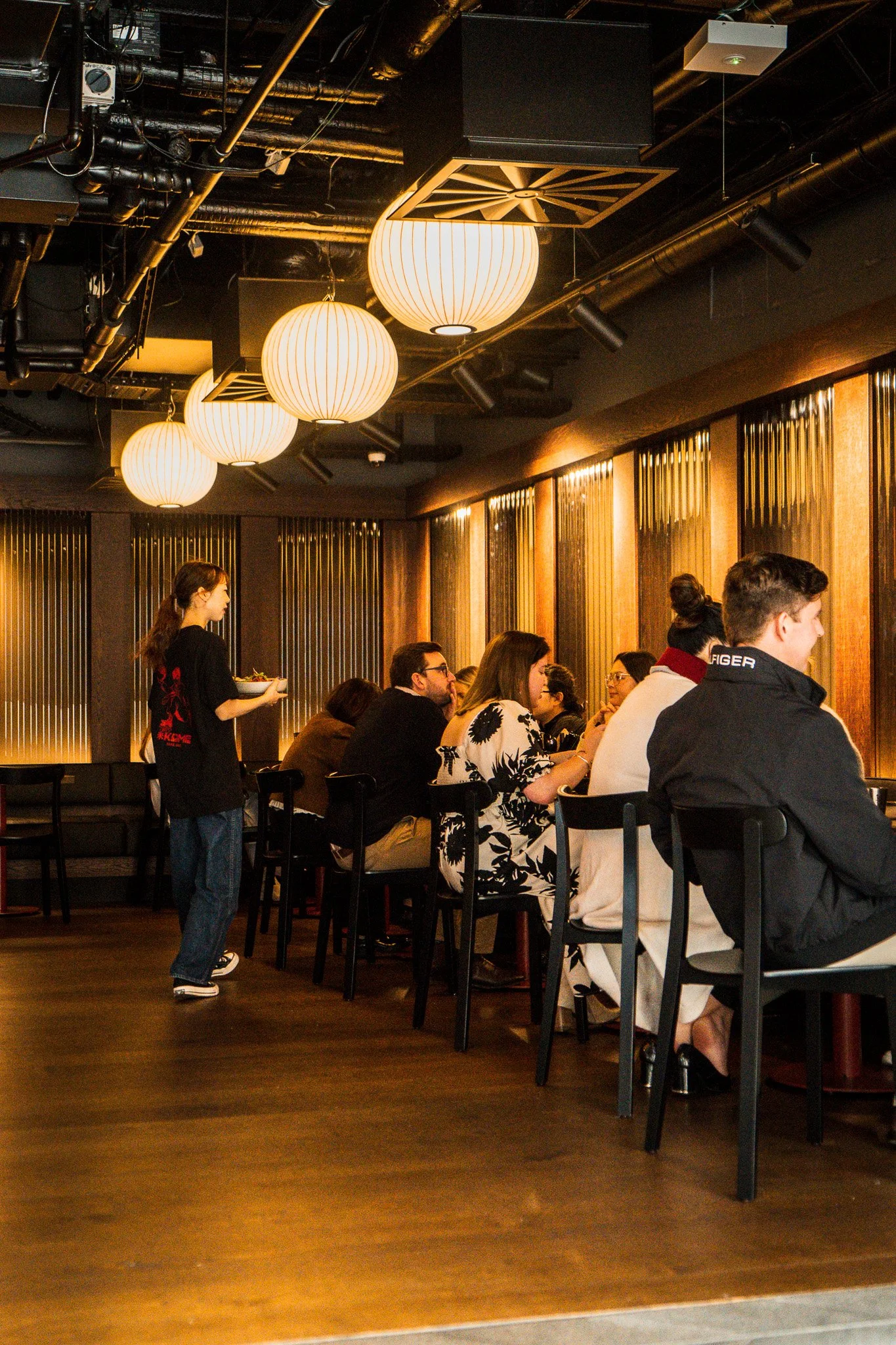 People dining at a restaurant with warm lighting, wooden wall accents, and modern decor.