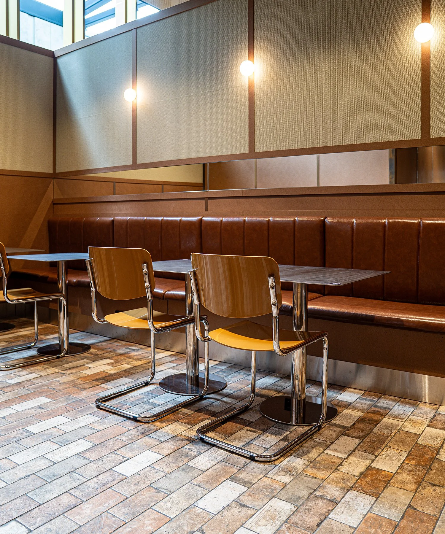 Empty restaurant booth with leather seating, wooden chairs, and brick flooring.
