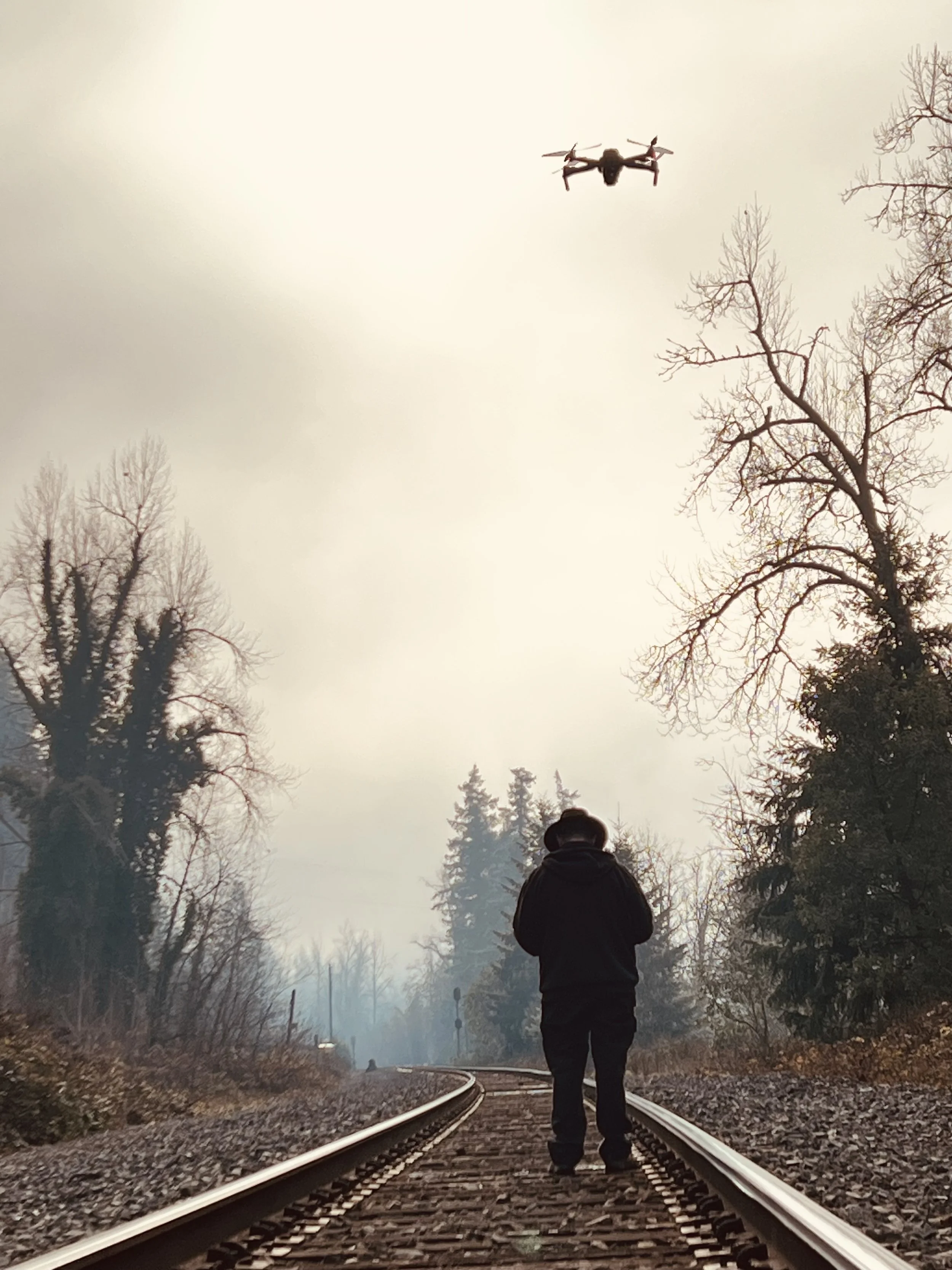 drone pilot standing on railroad tracks while drone flies above his head