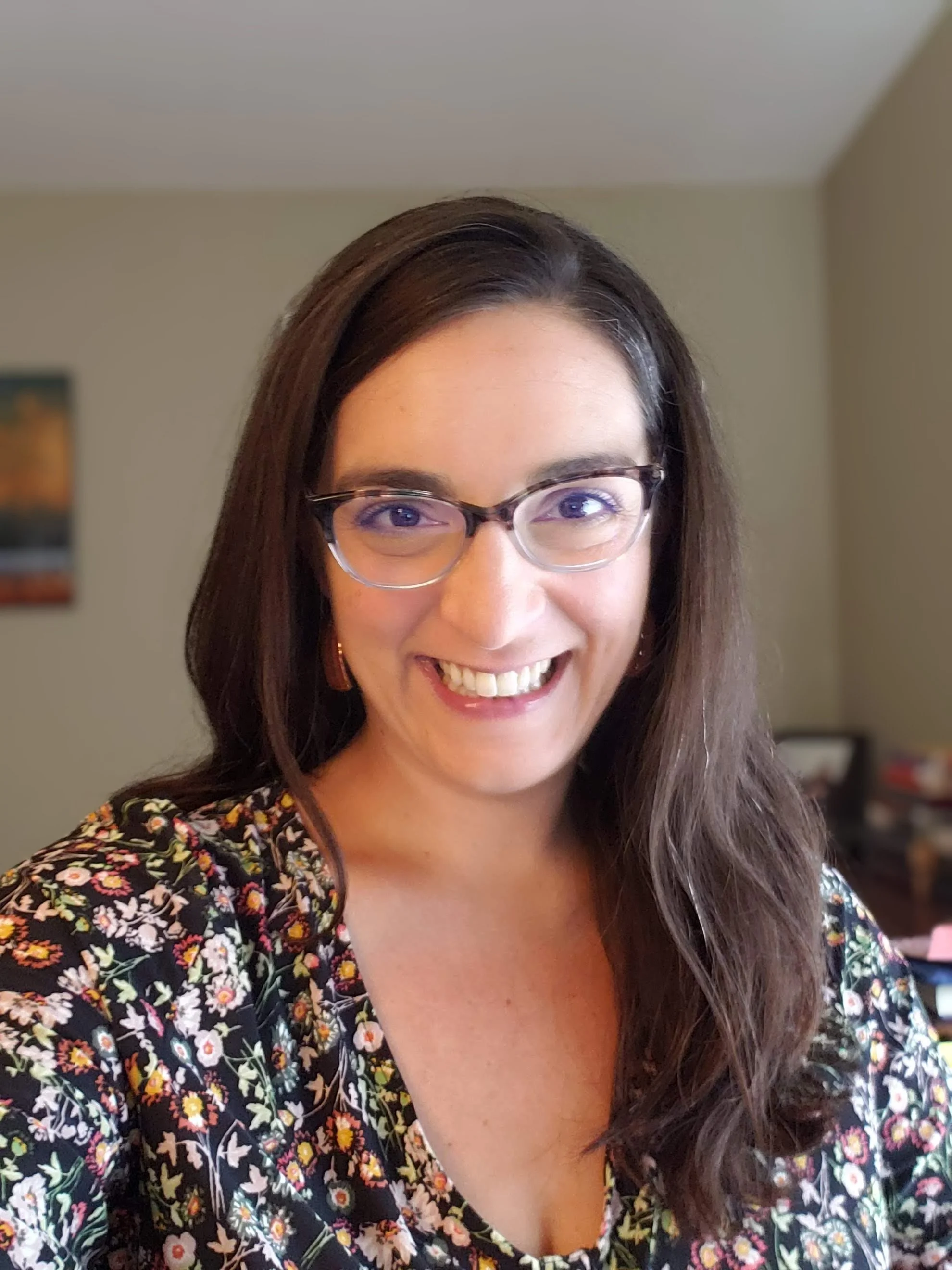WNDB development director Abbie Fine, a woman with long brown hair and glasses smiling in a room with beige walls and a floral dress.