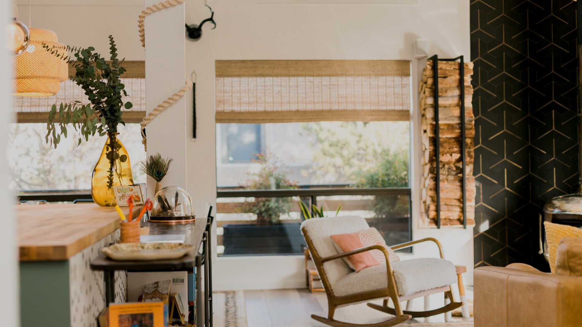 Living room with a rocking chair, decorative items, and a wood log holder near a large window with covered blinds.