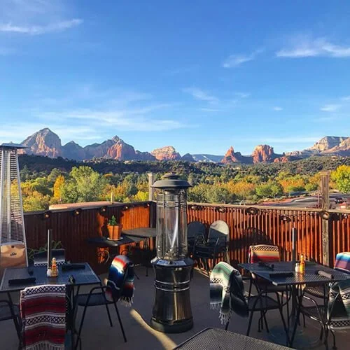 Rooftop patio with tables and chairs overlooking a landscape of trees and distant mountains under a blue sky.