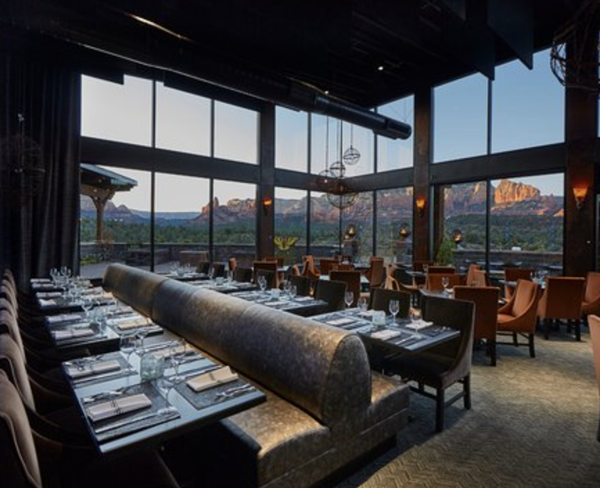 Elegant restaurant dining area with large floor-to-ceiling windows showcasing mountain views, set with tables, napkins, glasses, and silverware.