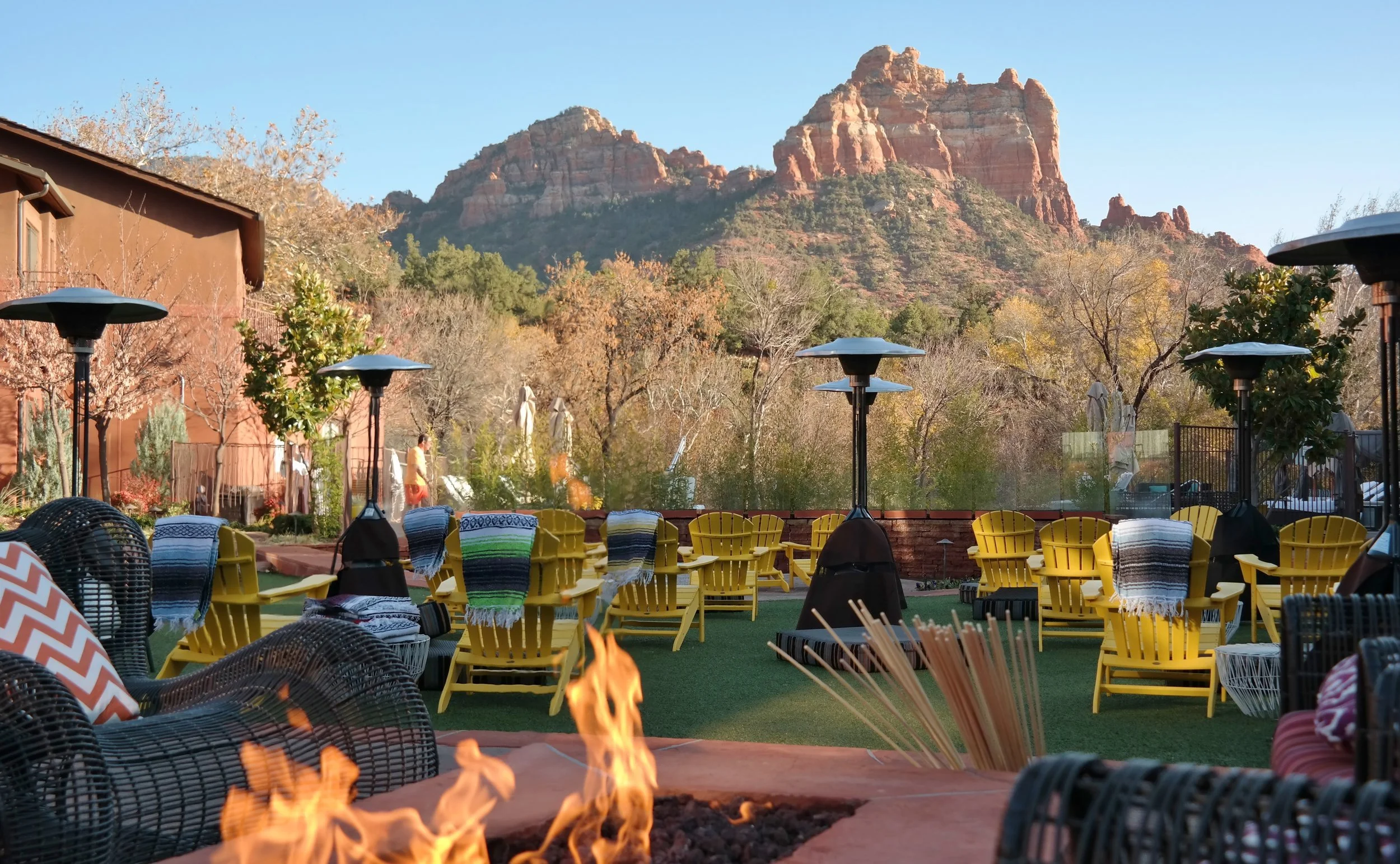 Outdoor patio area with yellow chairs, black patio heaters, a fire pit, and a mountain range in the background.