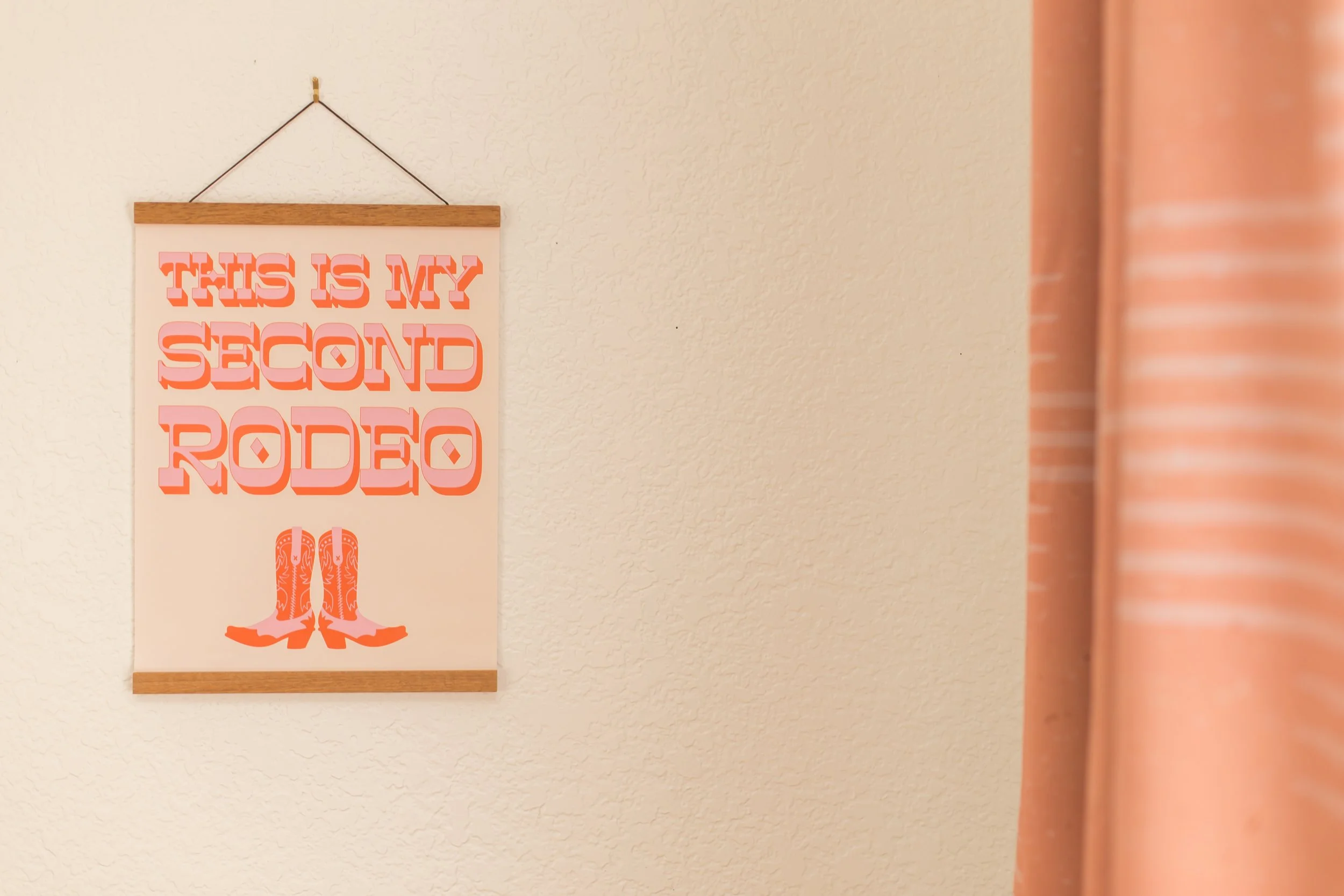 Poster on a wall with the text "This is my second rodeo" and an illustration of cowboy boots.