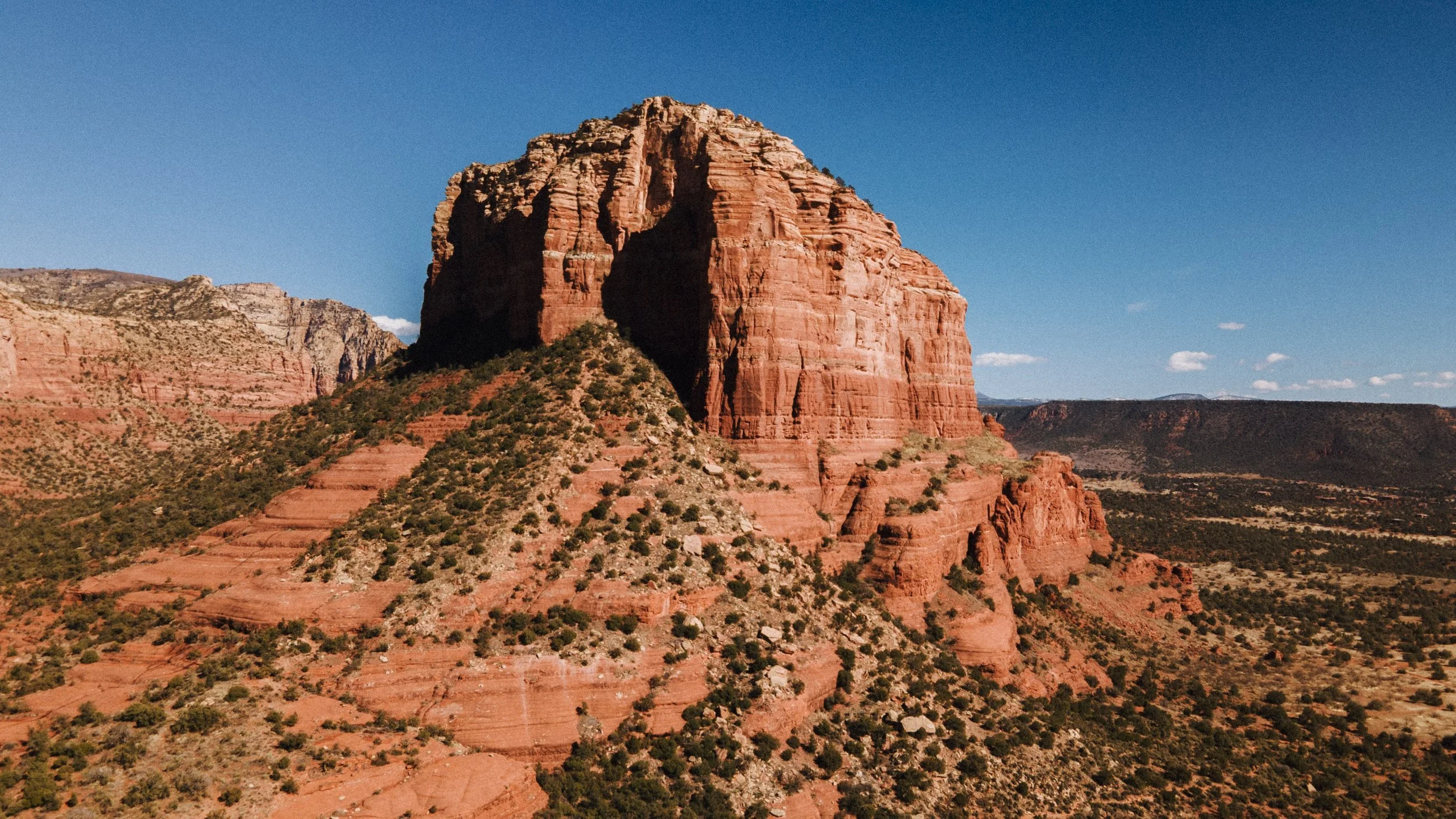 Red rock formation in a desert landscape under a clear blue sky with sparse clouds.
