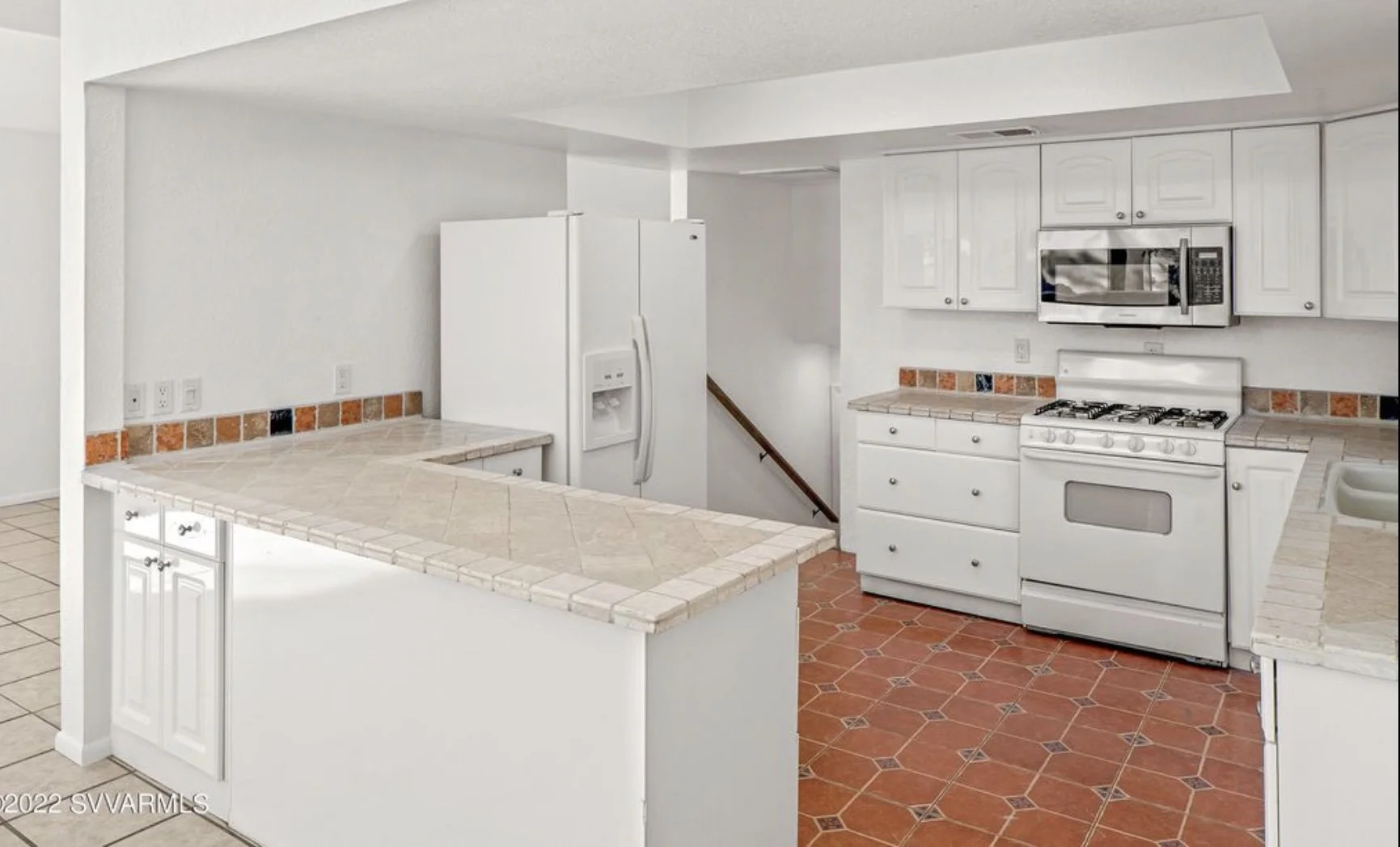 Kitchen with white cabinets, white refrigerator, microwave, stove, and tiled countertops and floors.