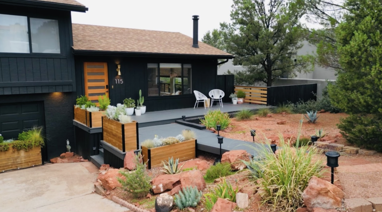 Front yard of a black house with a porch, outdoor seating, landscaped with desert plants, rocks, and pathway lighting.