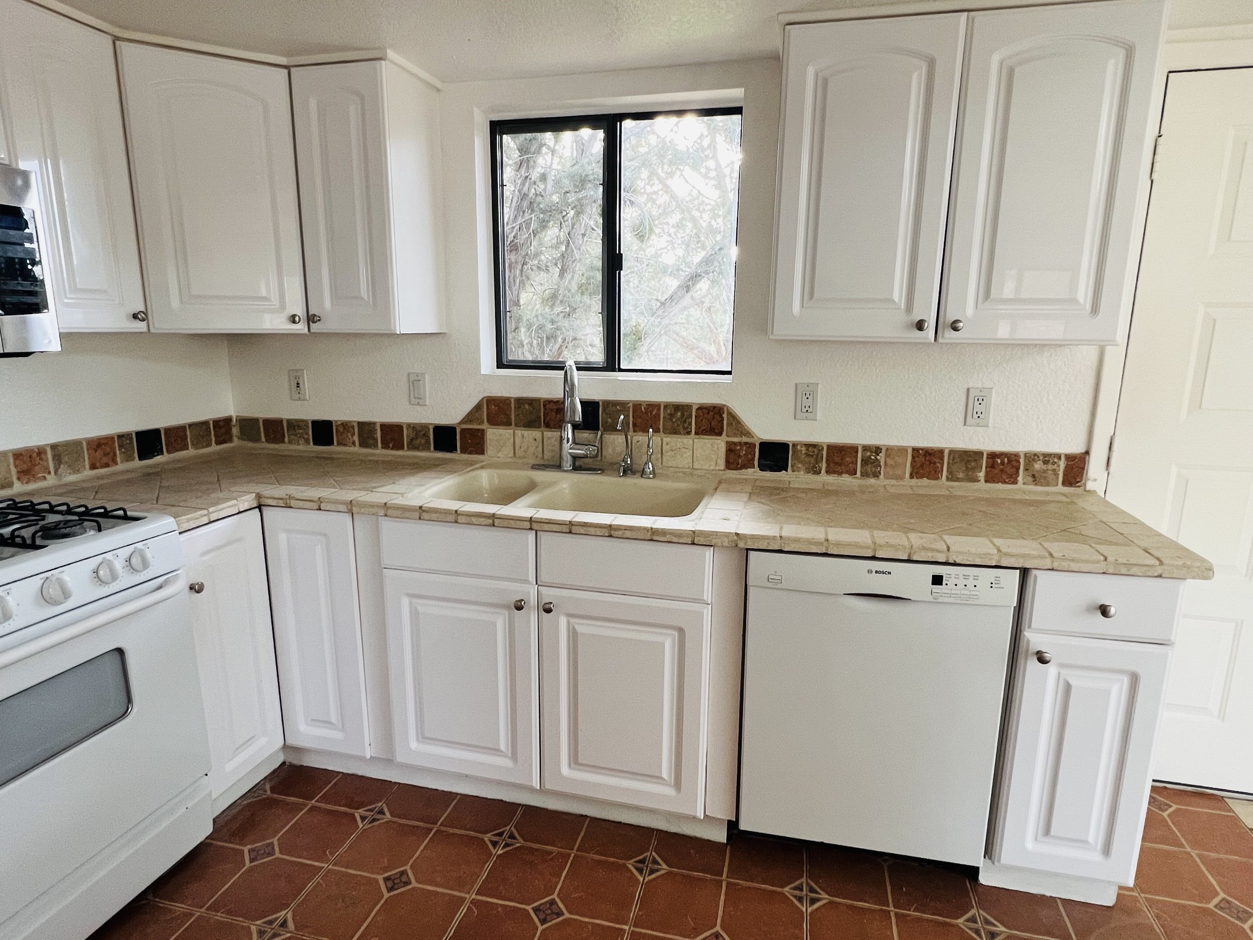 Kitchen with white cabinets, tiled beige countertops, a window above the sink, and a dishwasher.