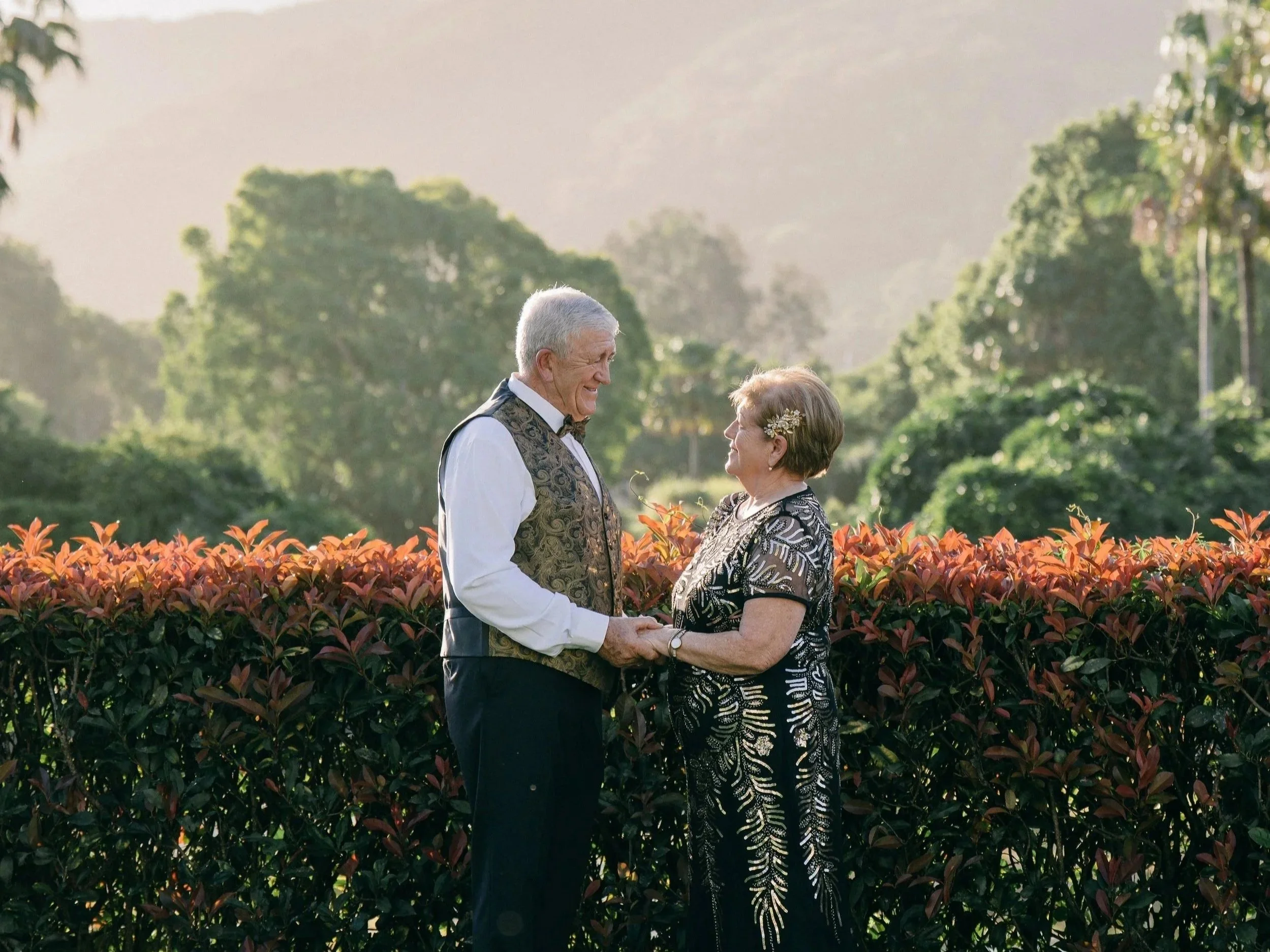 A couple in elegant attire sharing a kiss under a large tree on a grassy field.
