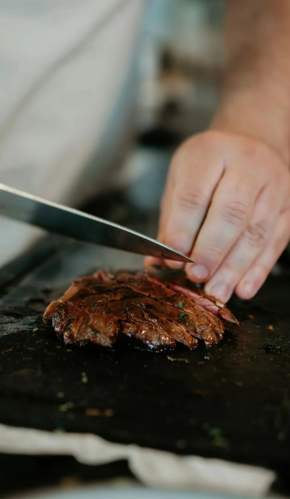 Close-up of a person slicing a cooked piece of meat with a knife on a black surface.