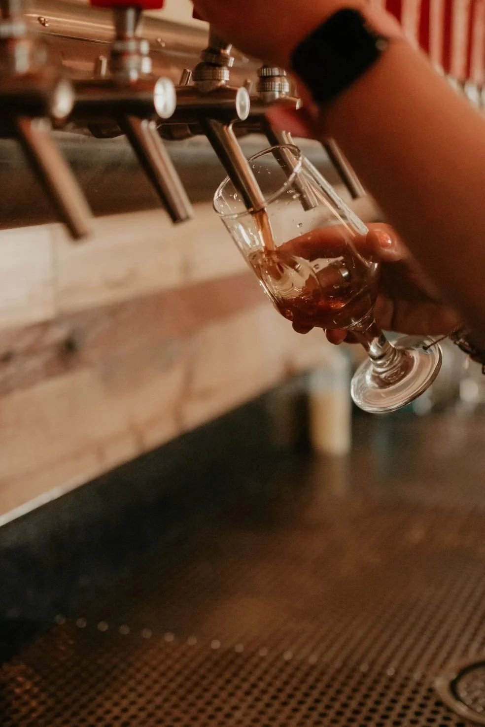 Person pouring draft beer into a wine glass at a bar.
