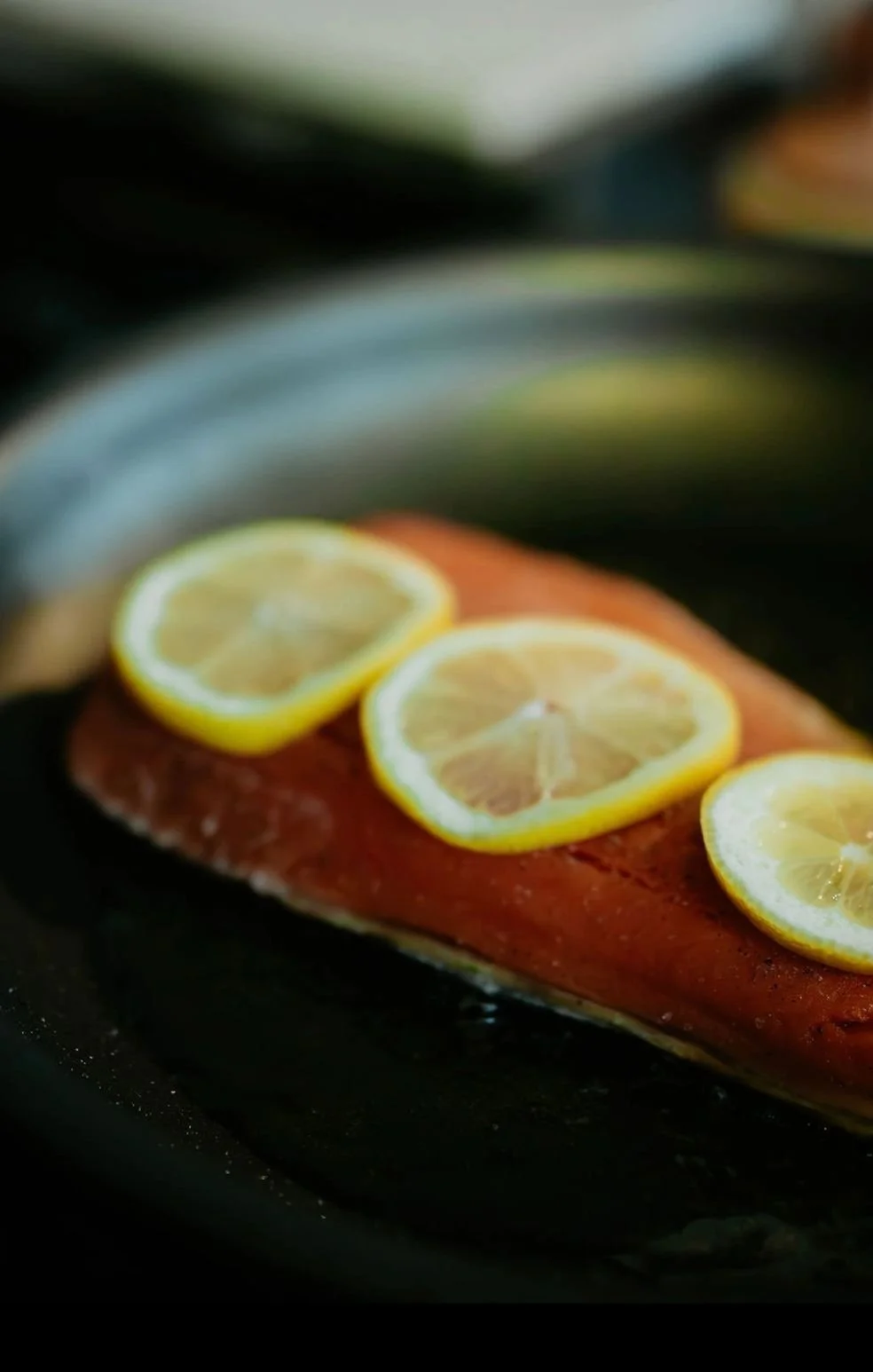 Raw salmon fillet topped with lemon slices on a black surface.