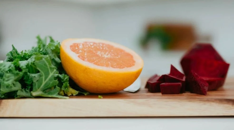 Half of an orange, chopped beets, and kale on a wooden cutting board.