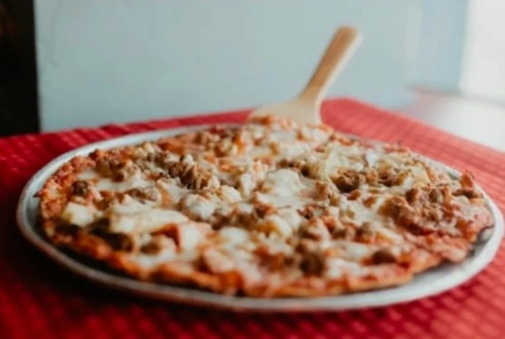 A plate of cheesy taco meat pizza on a wooden table with a red placemat.