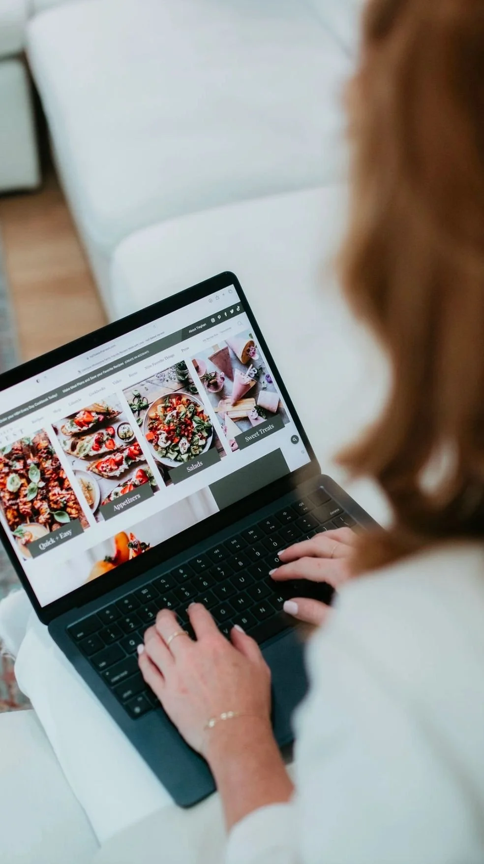 A woman browsing a food website on a laptop, viewing categories like Appetizers, Salads, Sweet Treats, and Quick & Easy.