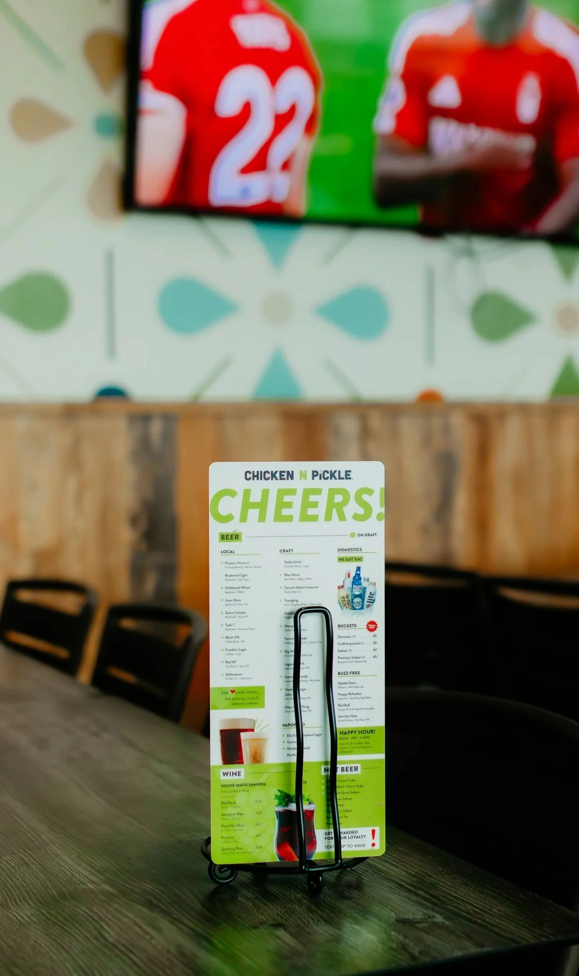 Menu card on a table in a restaurant, featuring beer and wine options, with a colorful wall and chairs in the background.