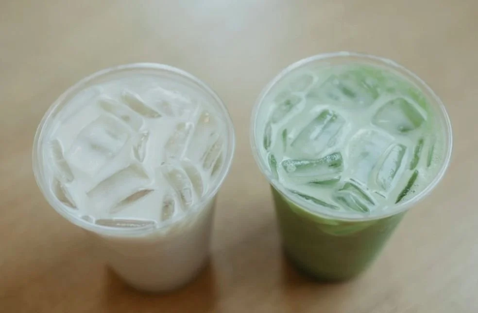 Two glasses of iced drinks, one with a milky white color and the other with a greenish hue, topped with ice cubes.