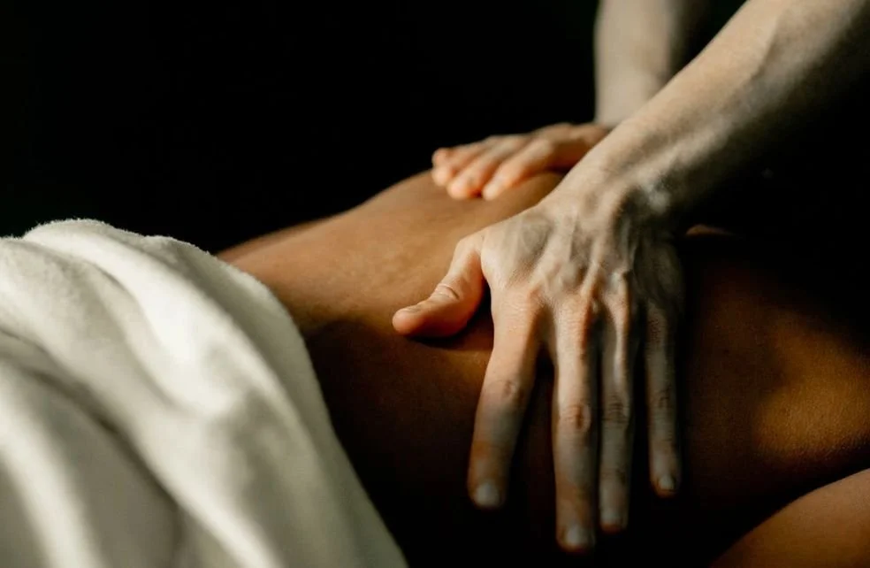Close-up of a person receiving a massage, with hands on their back, against a dark background.